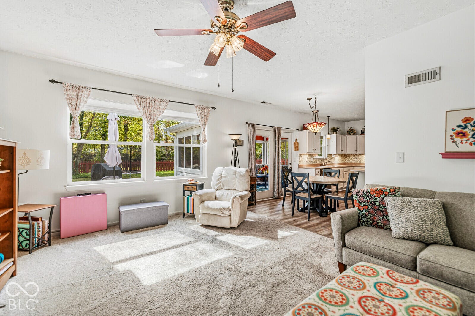 Open-concept interior featuring large windows, a ceiling fan with integrated lighting, wood-finish flooring, and glass-paneled exterior doors