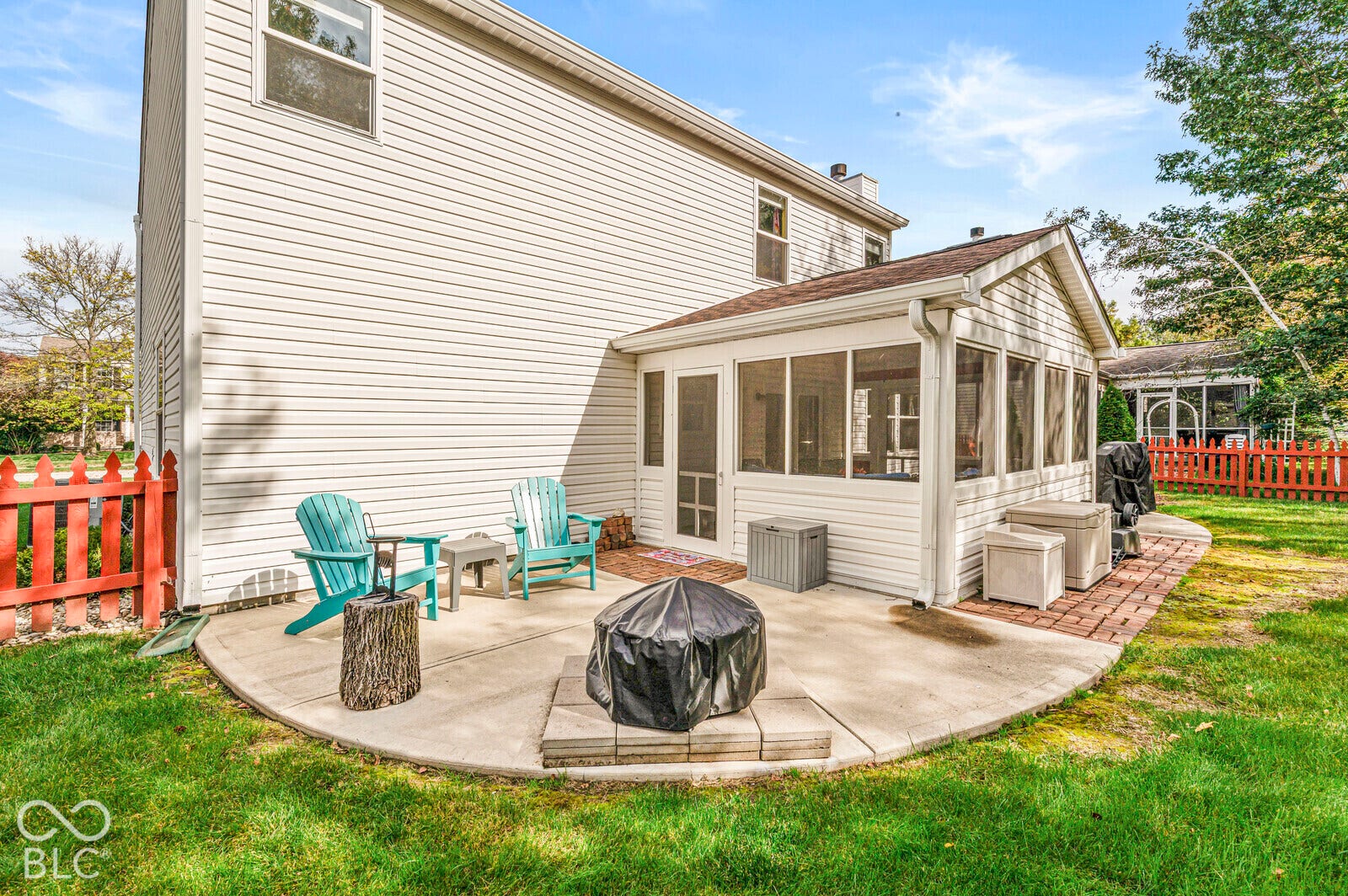 Rear exterior featuring vinyl siding, a screened-in porch with a gable roof, and a semi-circular concrete patio with brick border accents, enclosed by a perimeter picket fence