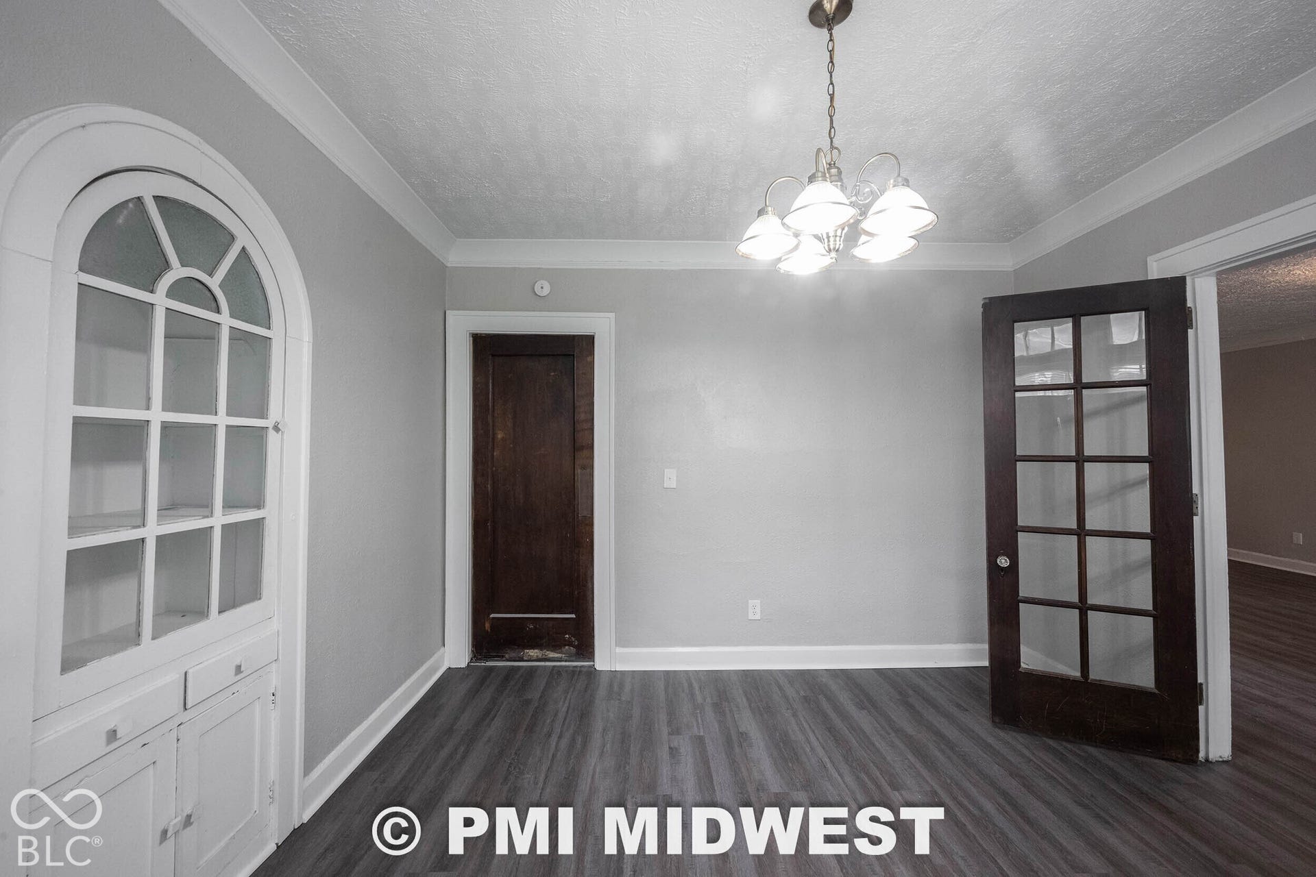 Wood-finish flooring, built-in arched display cabinetry, dark wood-finish interior door, and a multi-light chandelier