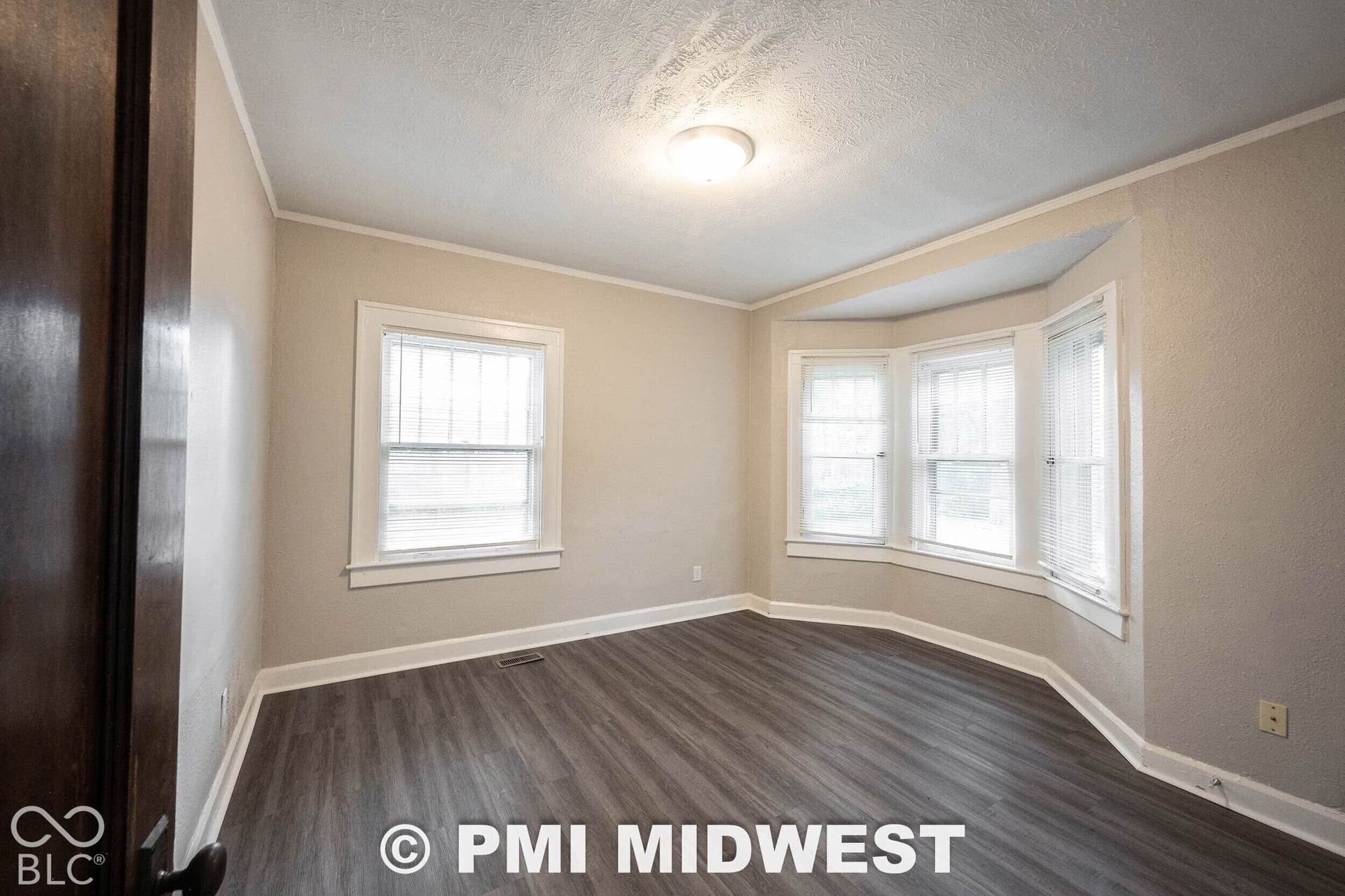Bay window with multiple panes, wood-finish flooring, neutral wall tones, and crown molding