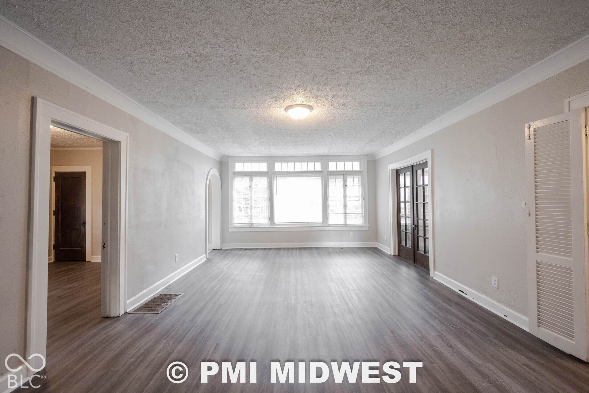 Spacious room featuring wood-finish flooring, a large multi-pane window, and double French doors