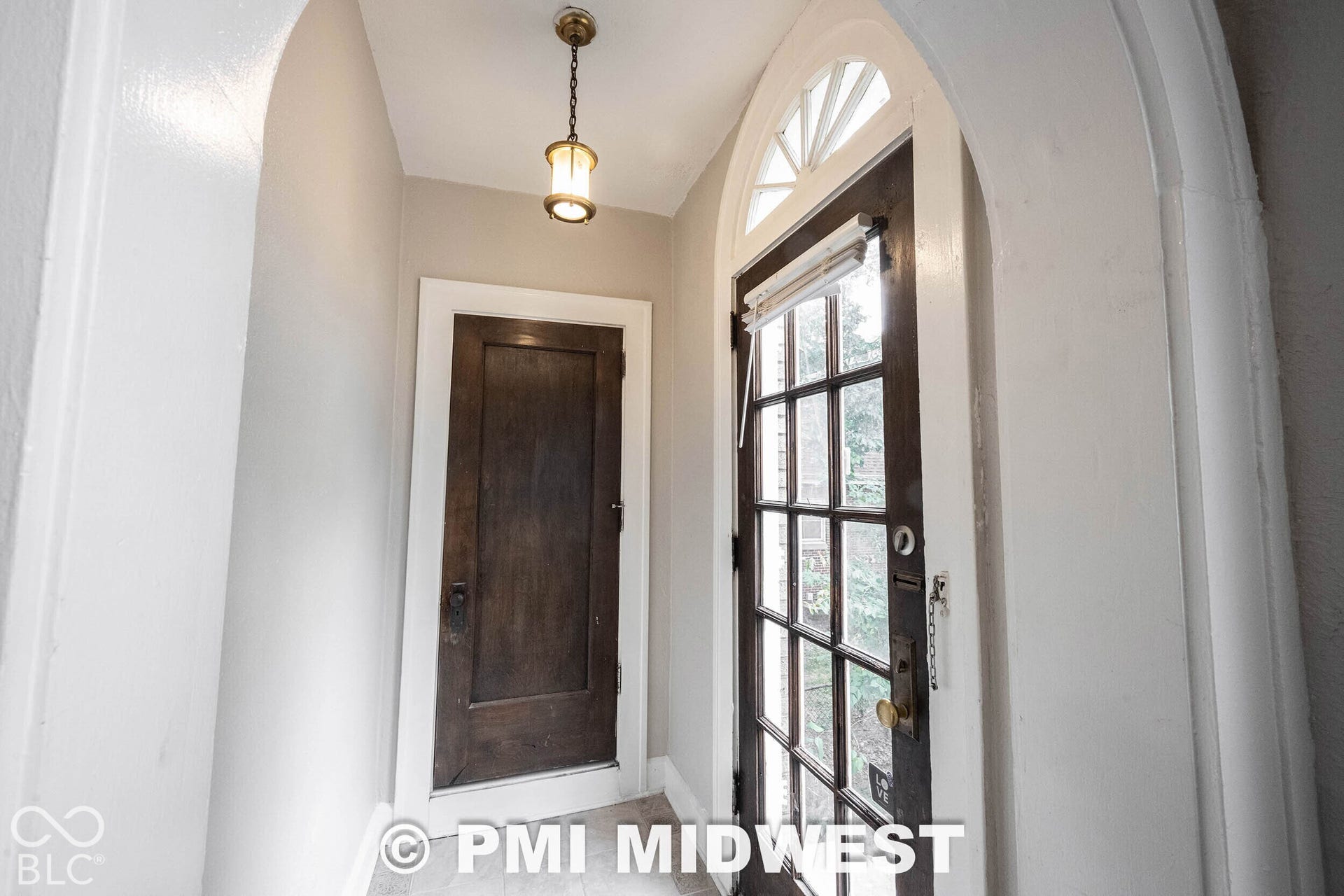 Arched entryway with a dark wood-finish door featuring a fanlight transom and a classic hanging pendant light fixture