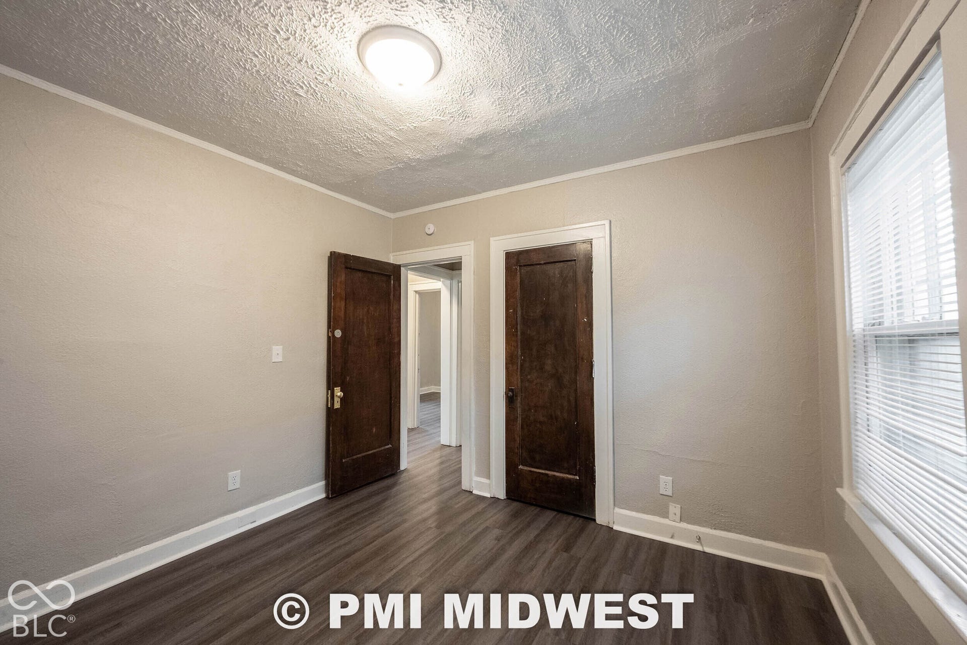 Wood-finish flooring with white baseboards, a textured ceiling with a flush-mount light fixture, and a window with blinds