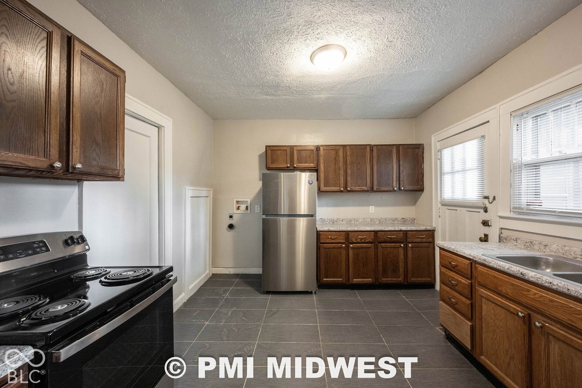 Kitchen featuring dark wood-finish cabinetry, a stainless steel refrigerator, a black electric range, a double basin sink, and tile flooring