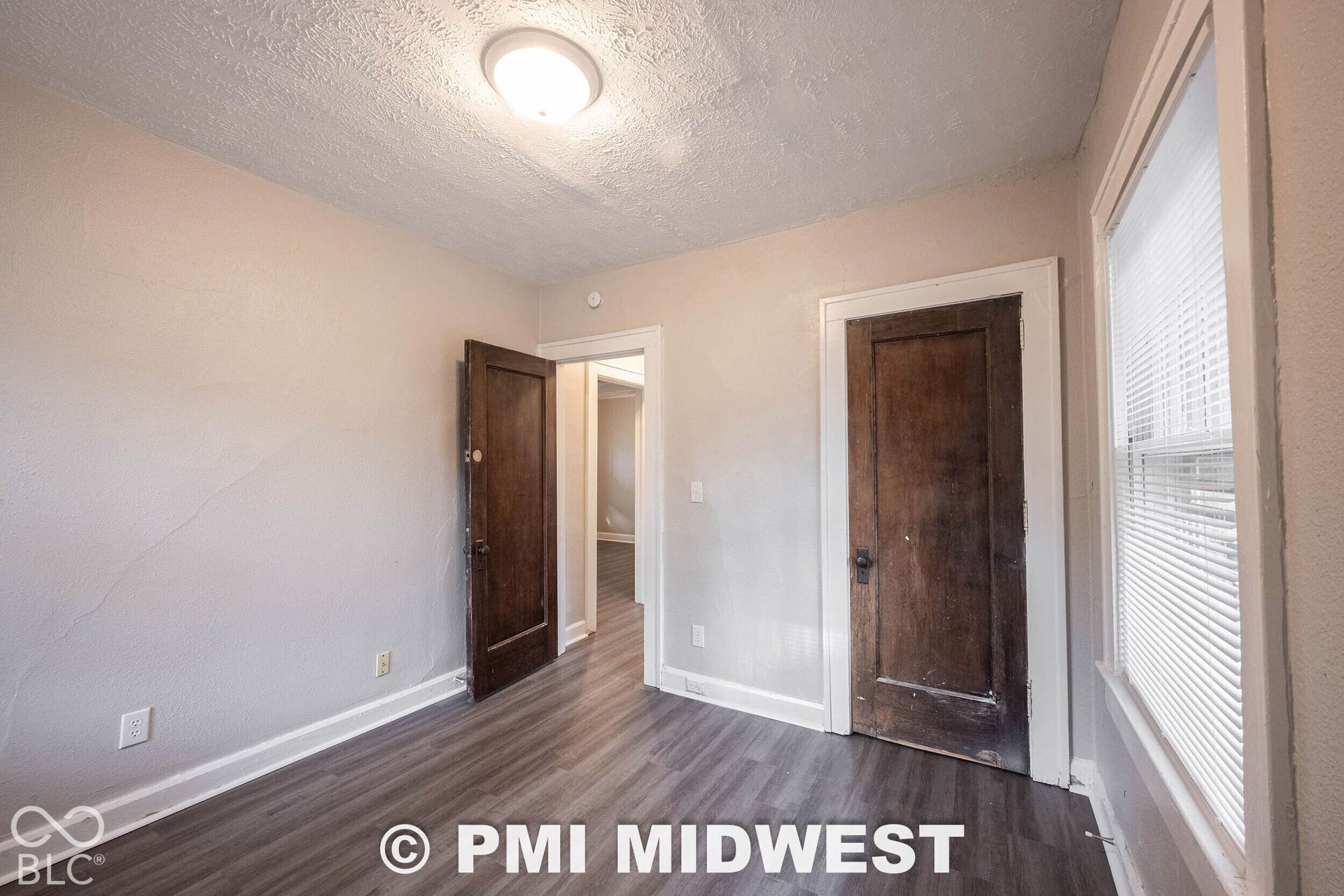 Wood-finish flooring, white trim, window with blinds, and ceiling-mounted light fixture