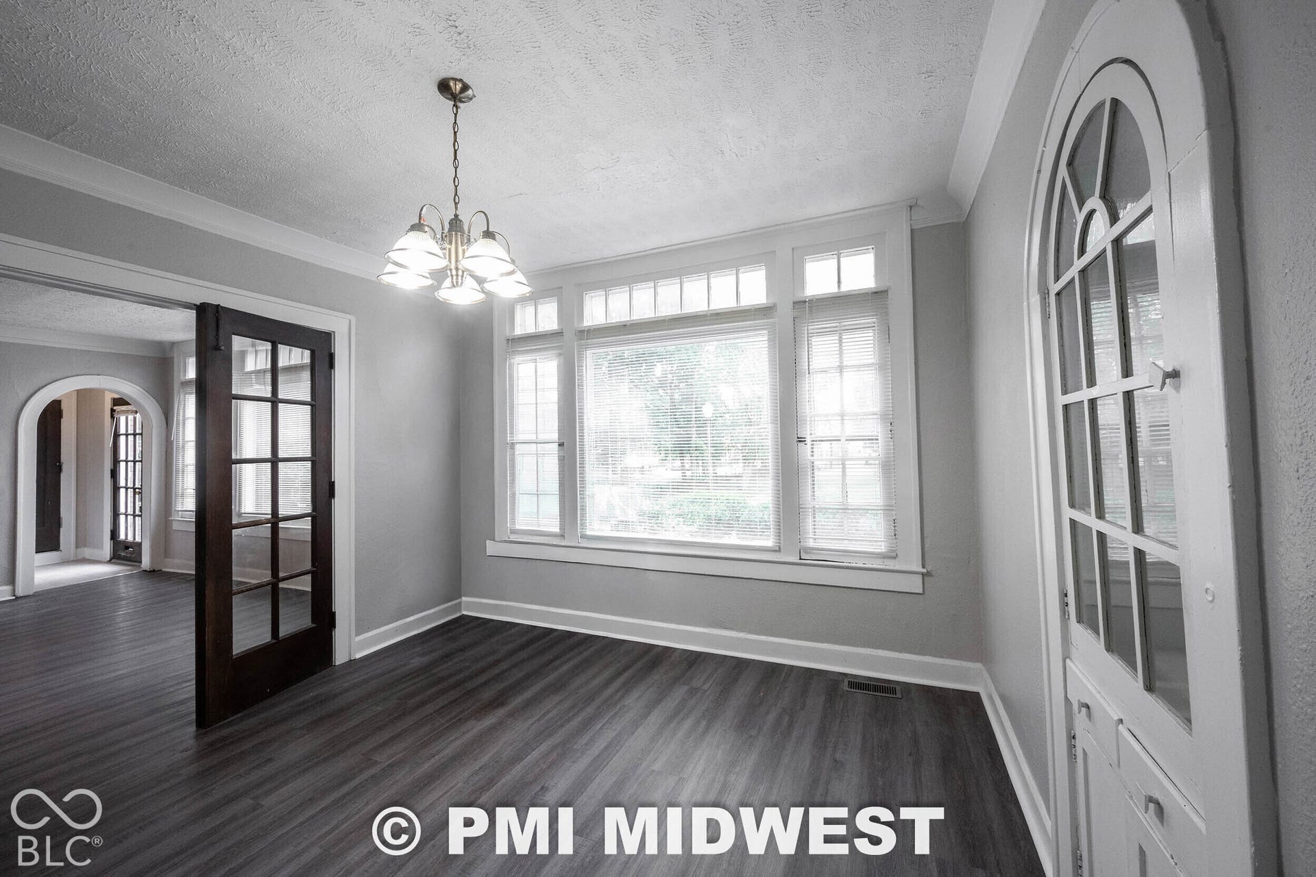 Spacious room featuring wood-finish flooring, a multi-pane window with transom lites, and a decorative arched door
