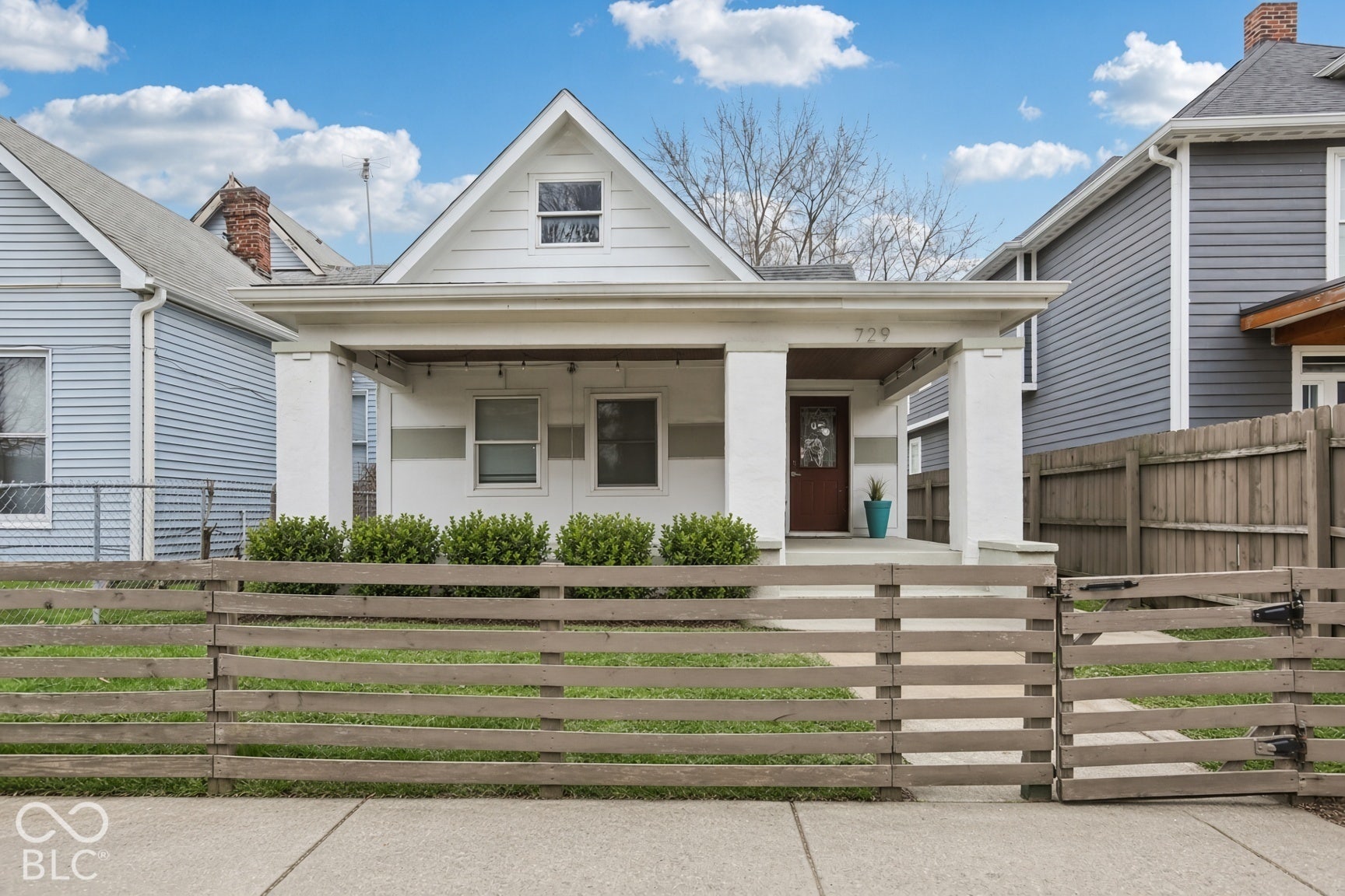 729 E Morris Street, Indianapolis, IN 46203 Gabled roofline, covered front porch, white siding, dark brown entry door, and low-slat wood fence