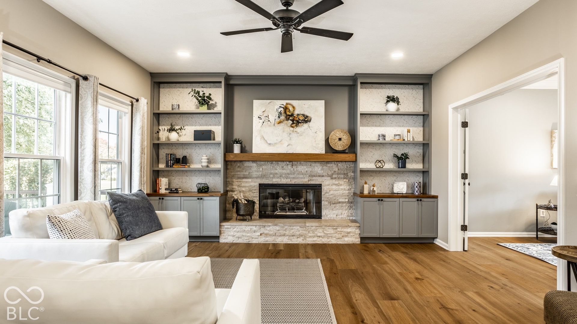 Stone-clad fireplace with a wood mantel, built-in shelving, wood-finish flooring, vaulted ceiling, and recessed lighting