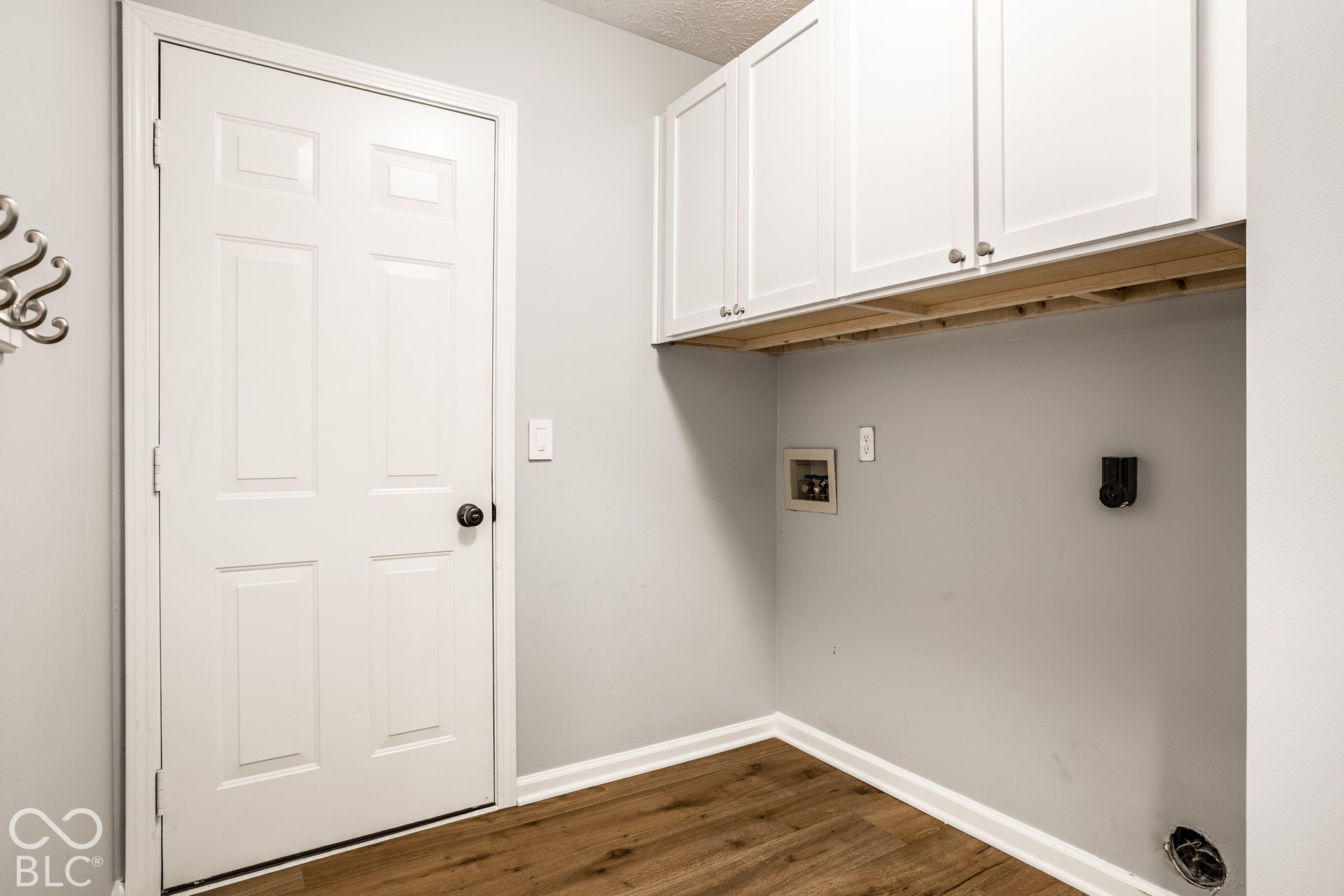 Laundry area with wood-finish flooring, overhead white cabinetry, and light gray walls