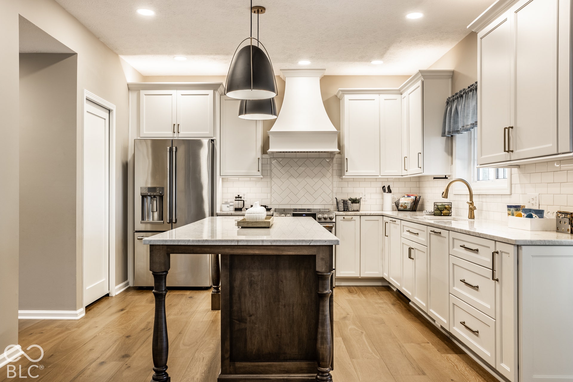 Kitchen featuring white shaker-style cabinetry, wood-finish flooring, a central island with a stone countertop, a stainless steel refrigerator, and a tile backsplash