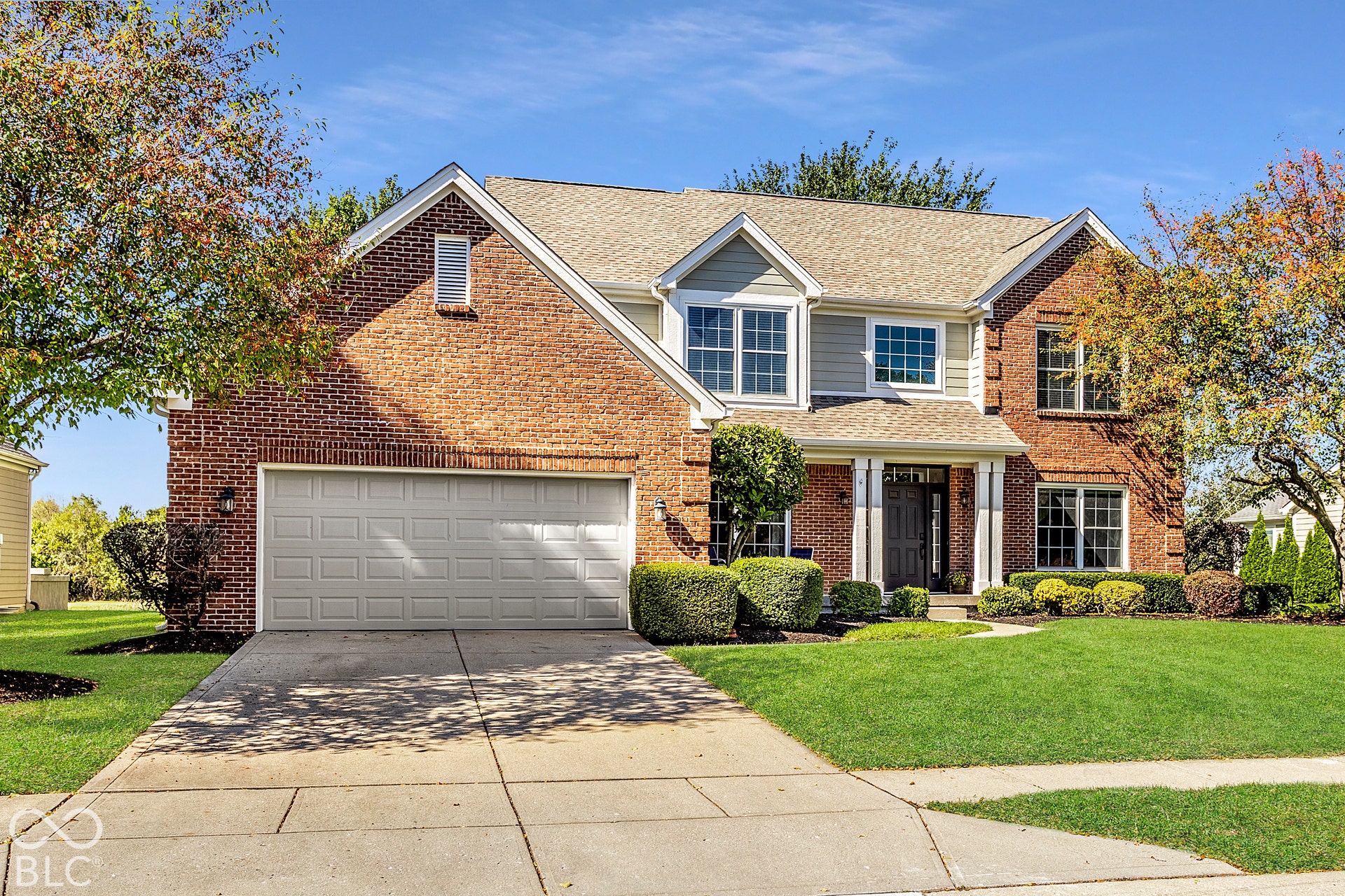 Brick and siding exterior, multi-pane windows, front door with sidelights, attached garage, and manicured landscaping