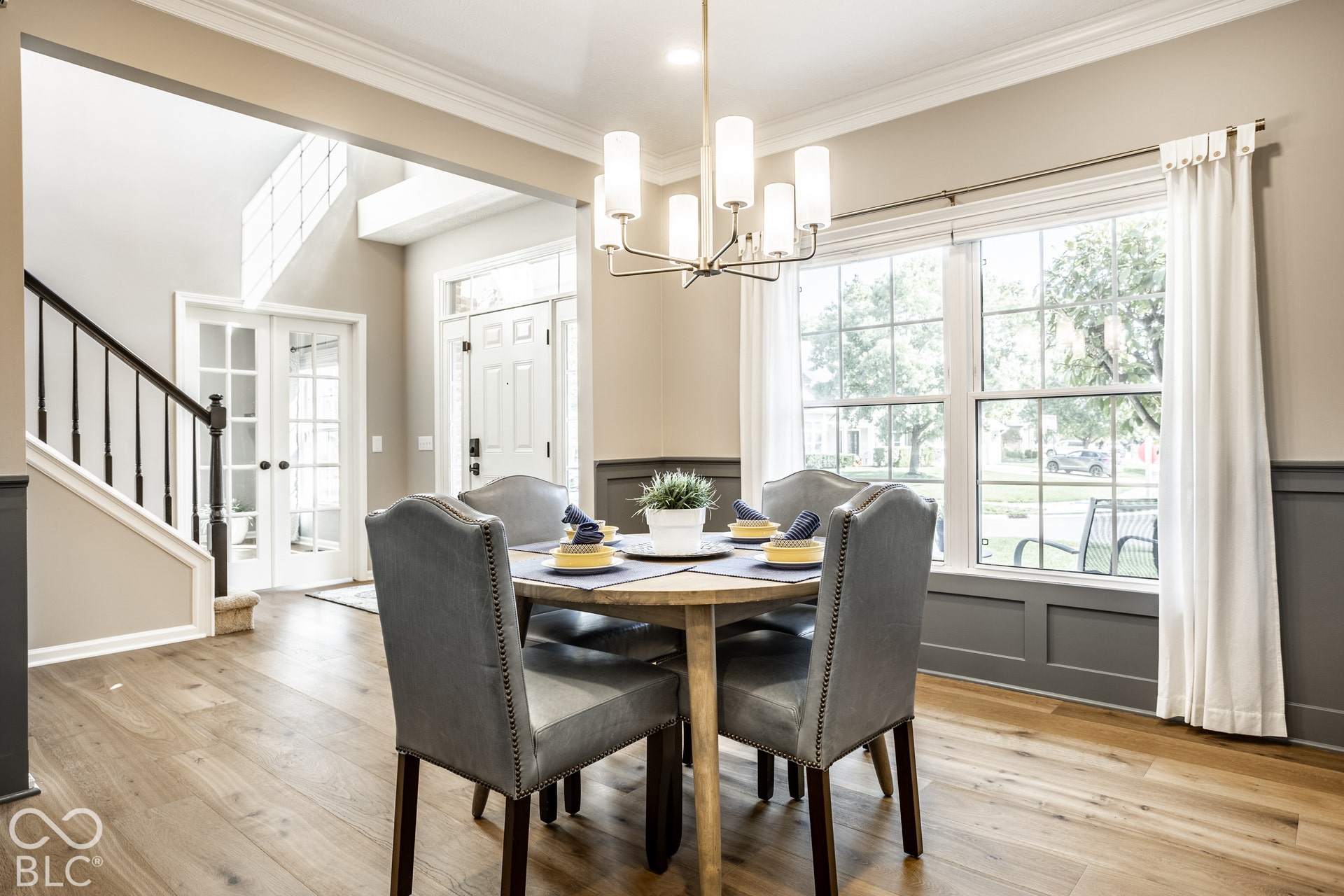 Wood-finish flooring, paneled wainscoting, a contemporary chandelier, large windows, and crown molding
