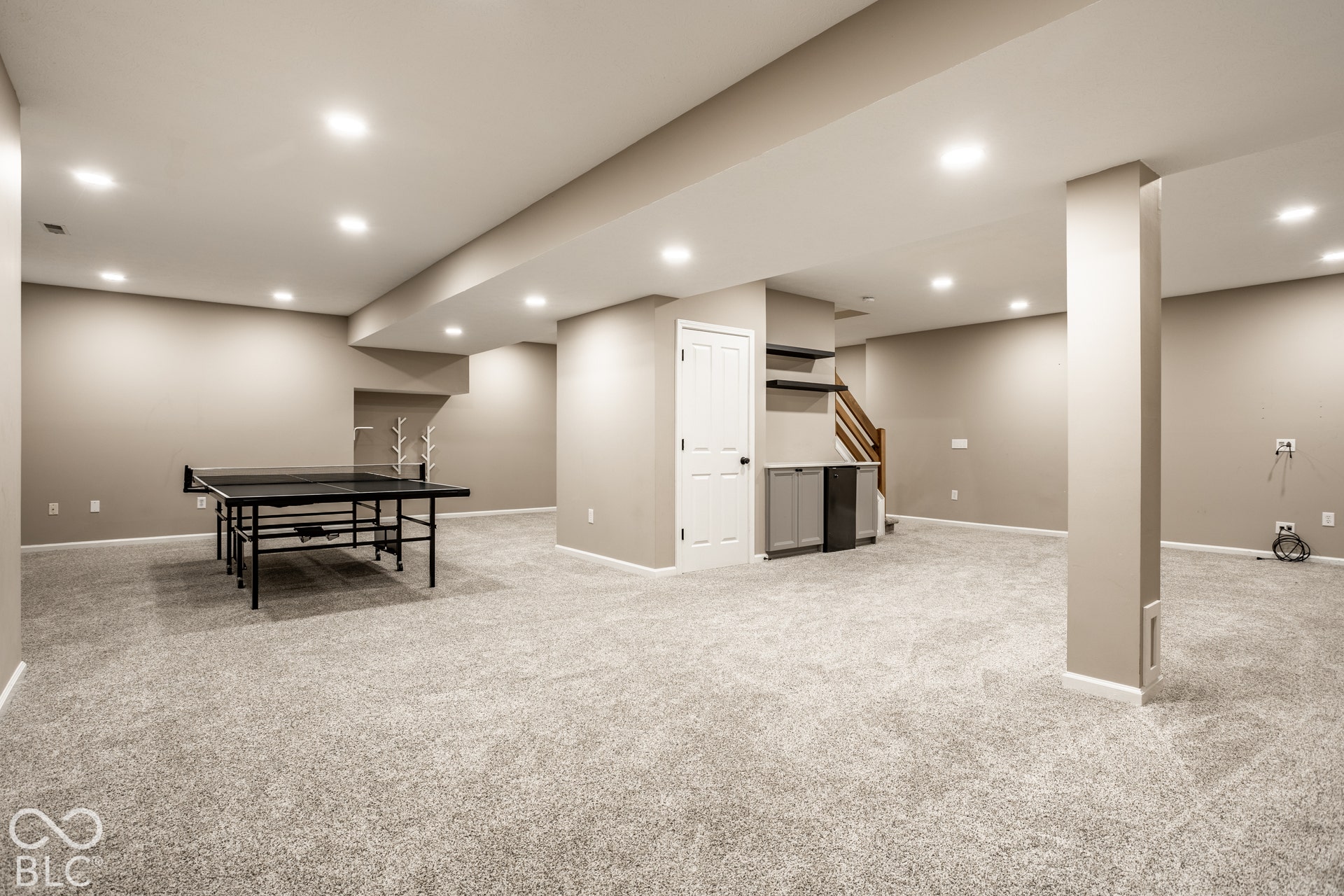Expansive carpeted area with recessed lighting, built-in shelving, and a beverage cooler