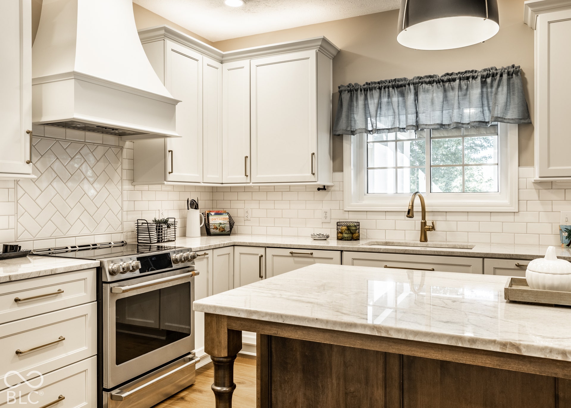 White shaker cabinetry, light-toned countertops, stainless steel range, tile backsplash, and a window above the sink