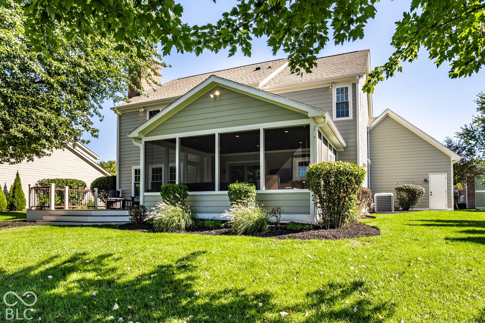 Expansive green lawn, screened porch, mature landscaping, and light gray siding