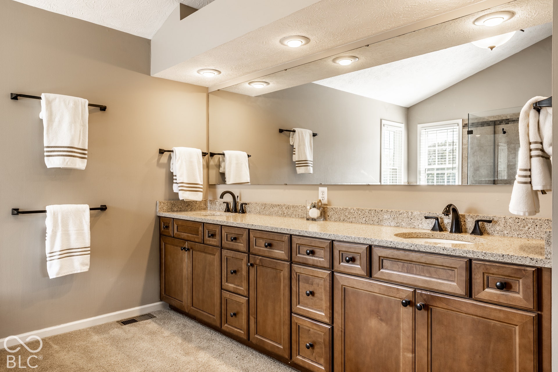 Dual vanity with wood-finish cabinetry, light speckled countertop, and matte black fixtures
