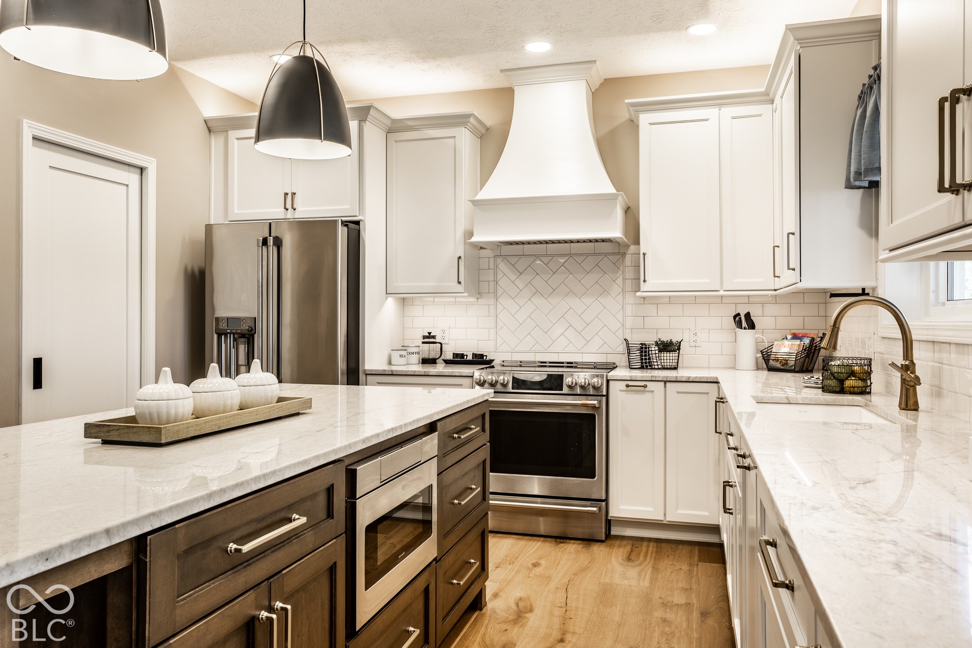 Kitchen featuring a large island with built-in microwave, white cabinetry, herringbone tile backsplash, and wood-finish flooring