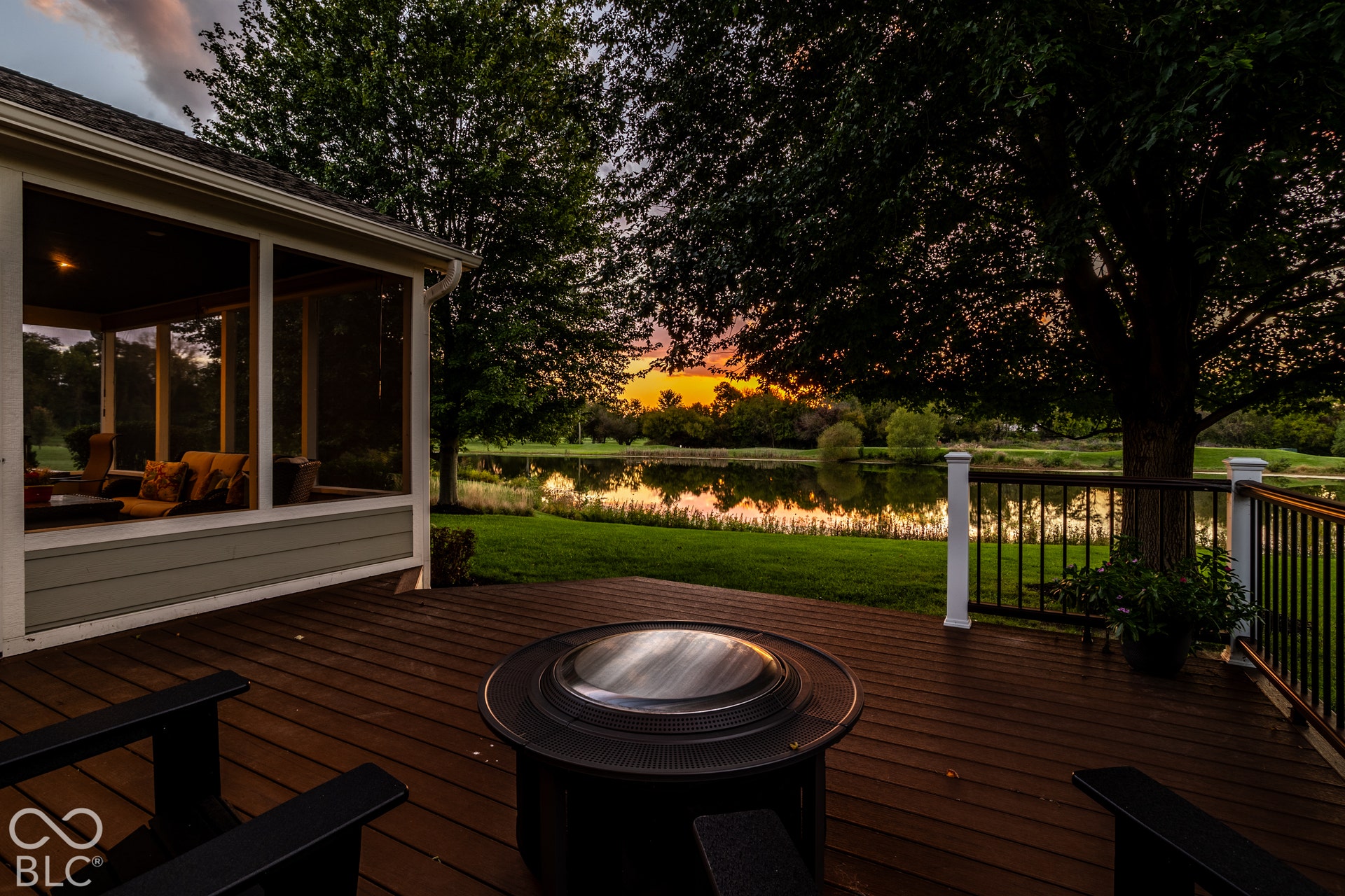 Screened-in porch, expansive deck, metal railing with white posts, lush green lawn, and a serene body of water