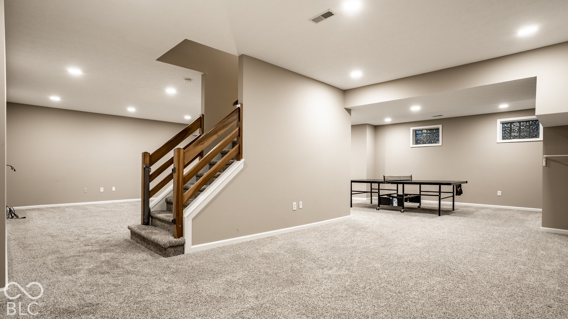 Expansive carpeted area featuring recessed lighting, a finished staircase with wood railing, and two egress windows