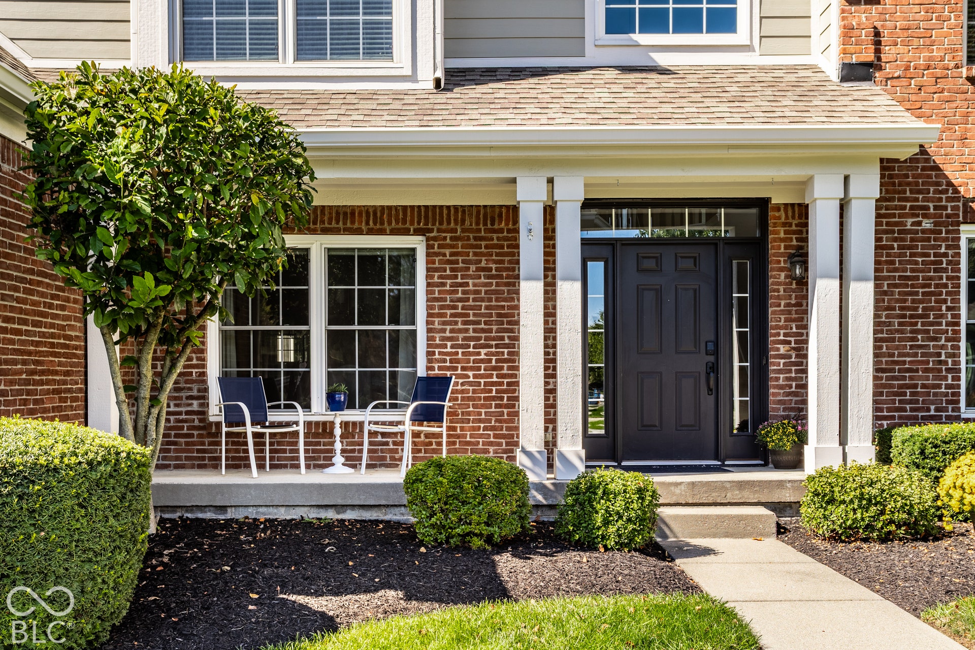 Brick facade with white trim, covered front porch, concrete pathway, and mature landscaping