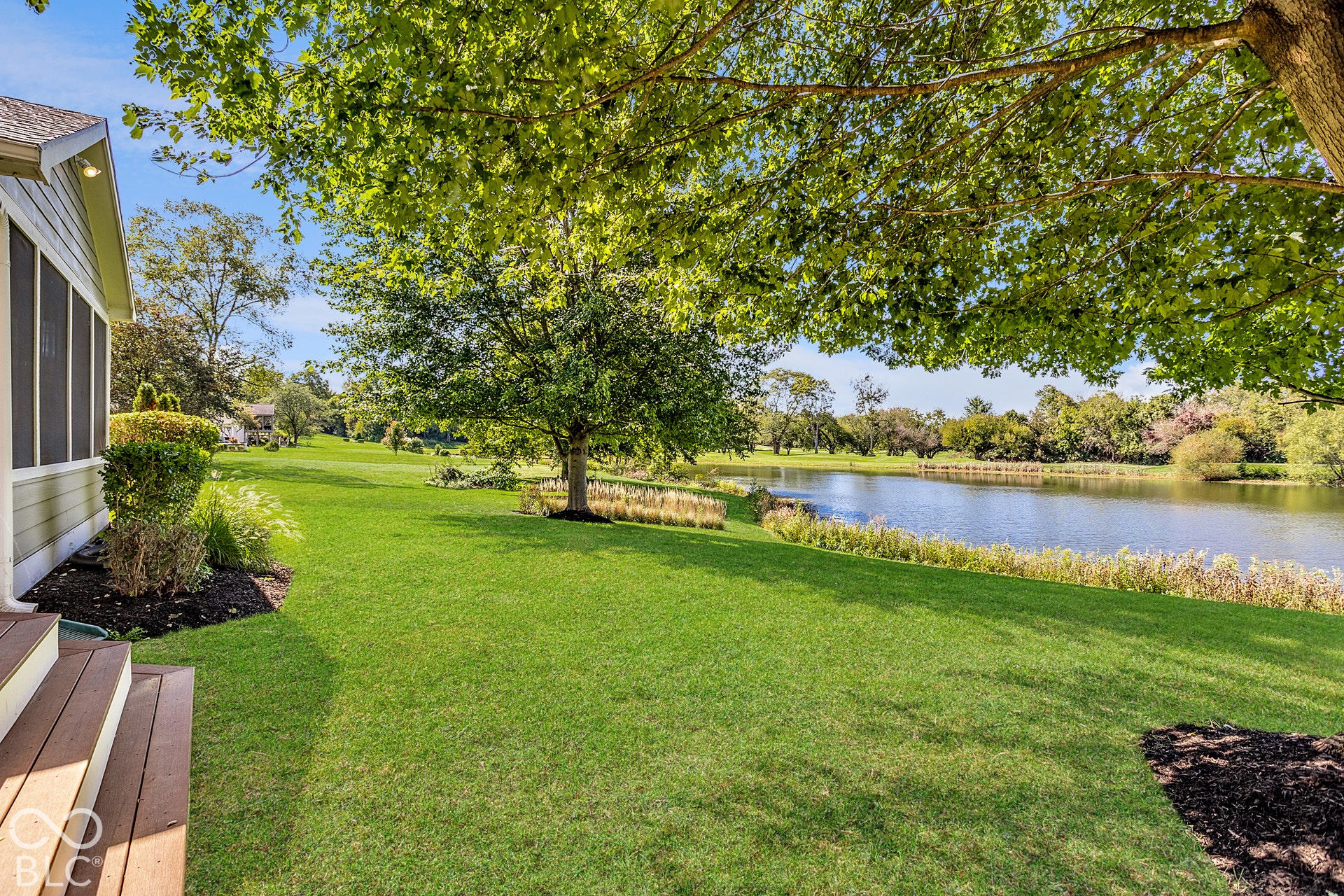 Expansive green lawn extending to a body of water, mature tree providing shade, and a screened-in porch