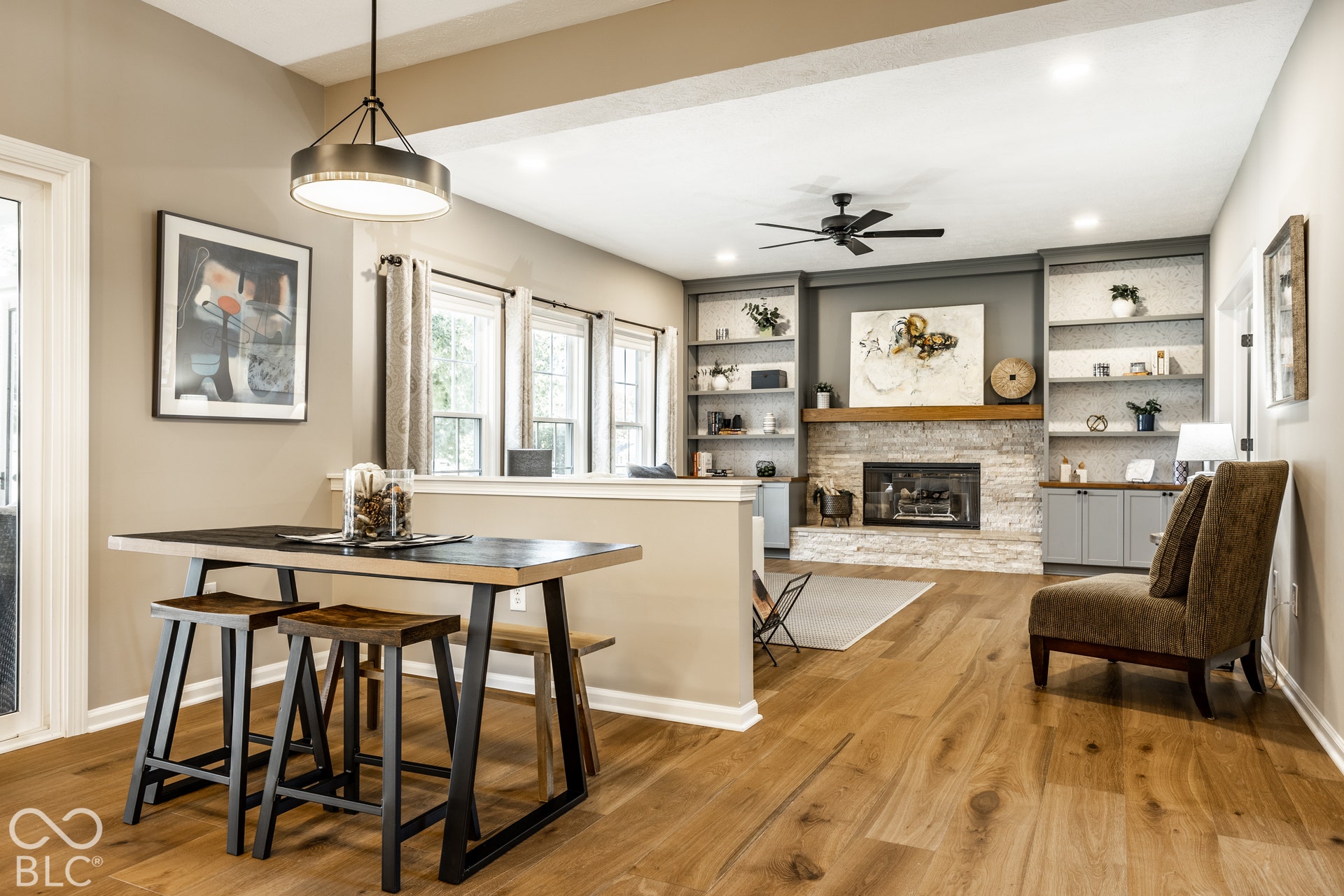 Hardwood-finish flooring throughout, featuring a stone-clad fireplace with a wood mantle, built-in shelving, and a ceiling fan