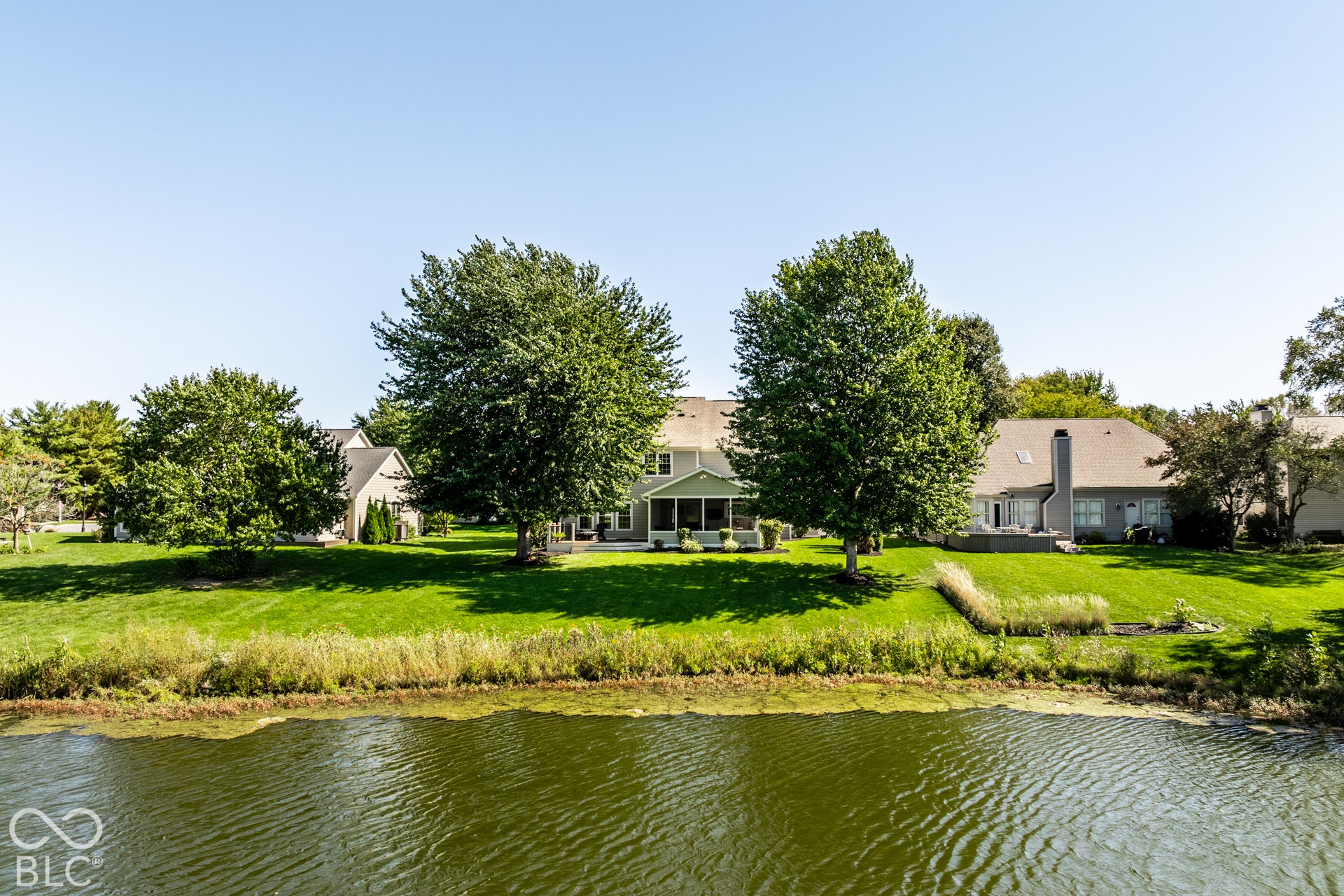 Expansive green lawn with mature trees, a screened-in porch, and a waterside setting
