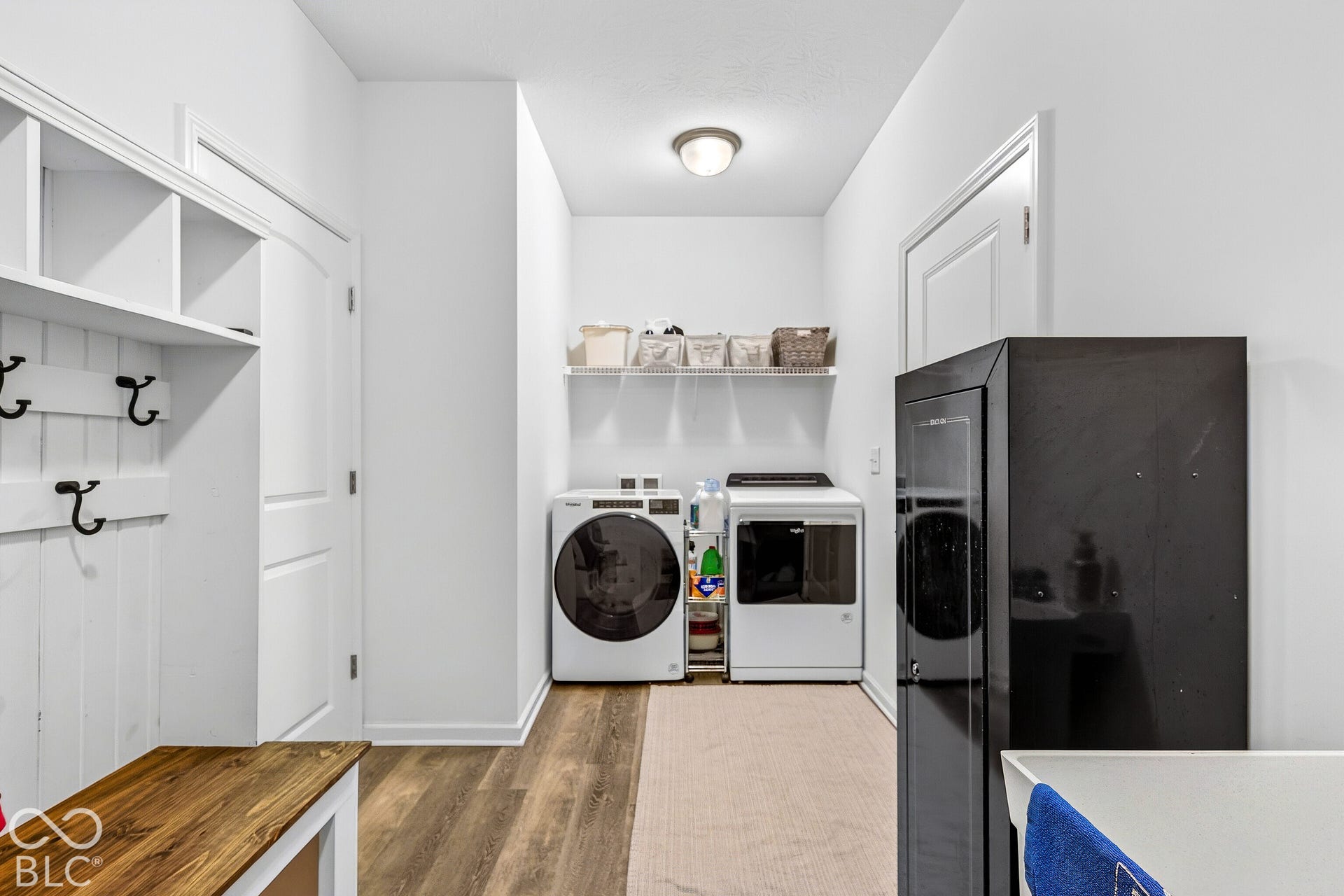 Built-in storage shelves, wall-mounted coat hooks, and wood-finish flooring in a bright utility space