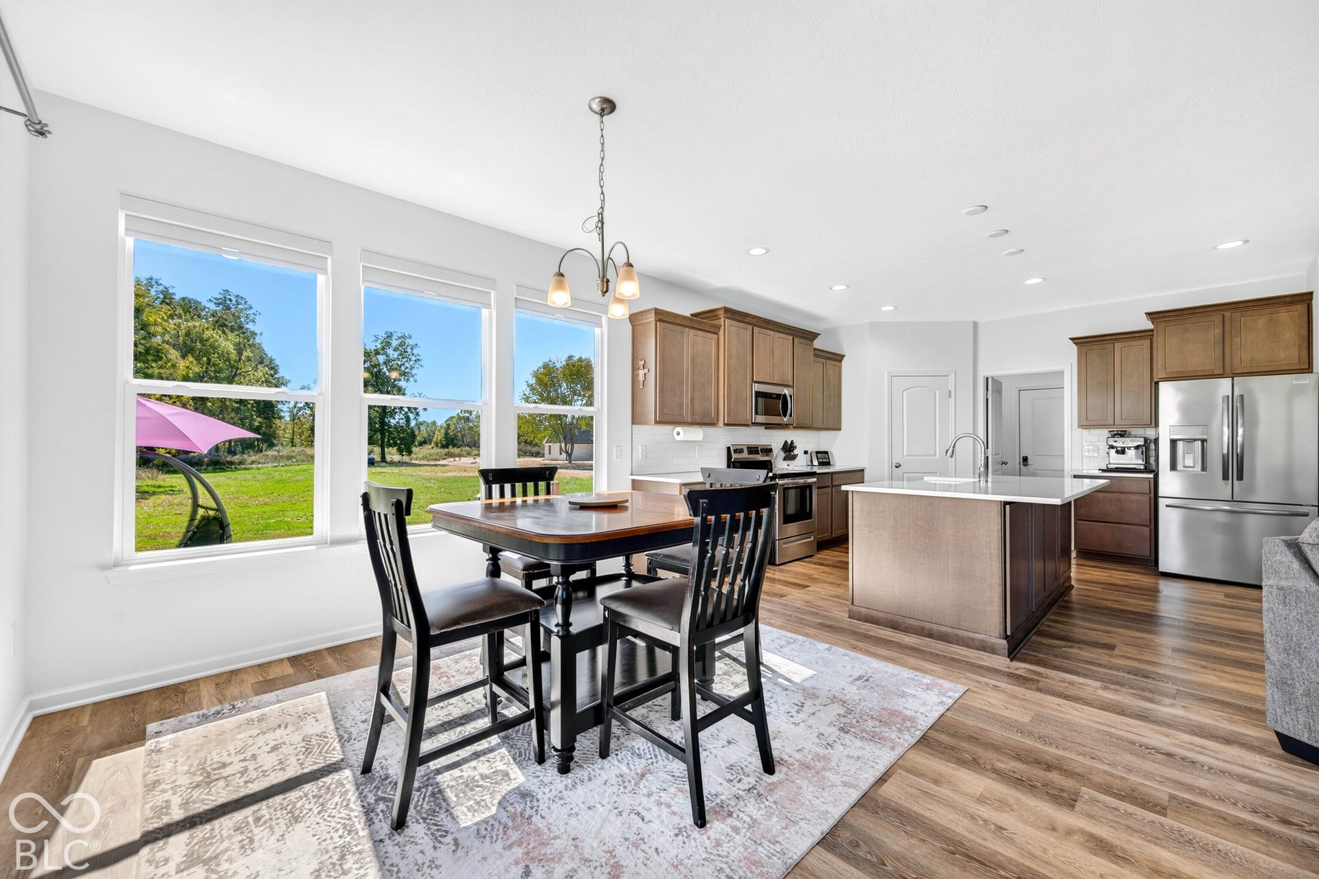 Three large windows, wood-finish flooring, recessed lighting, and a kitchen island with a built-in sink