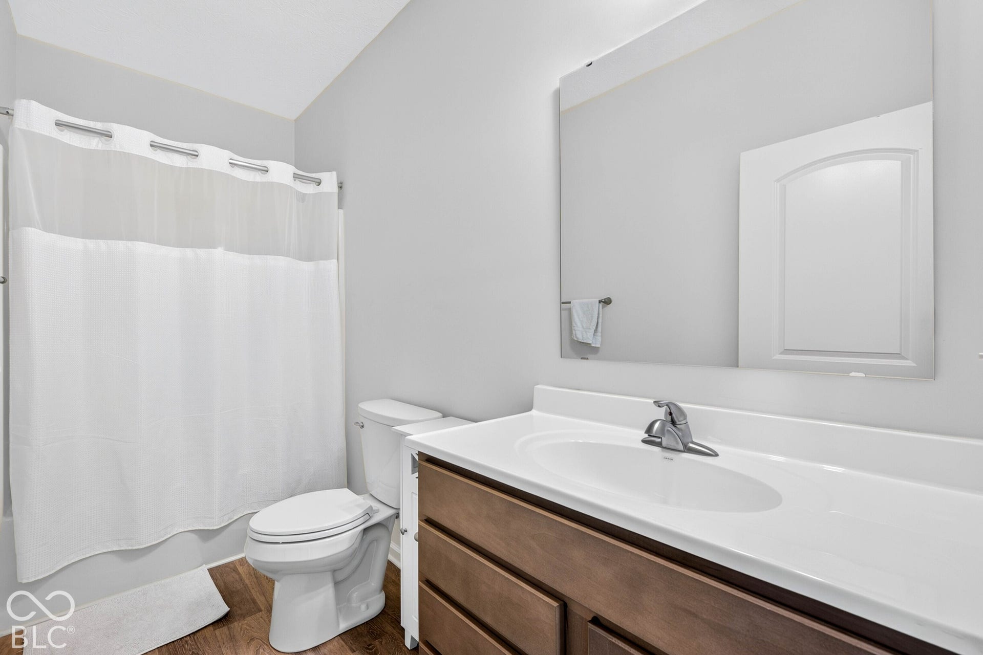Wood-finish flooring, single vanity with integrated sink, chrome faucet, white countertop, and wall-mounted mirror