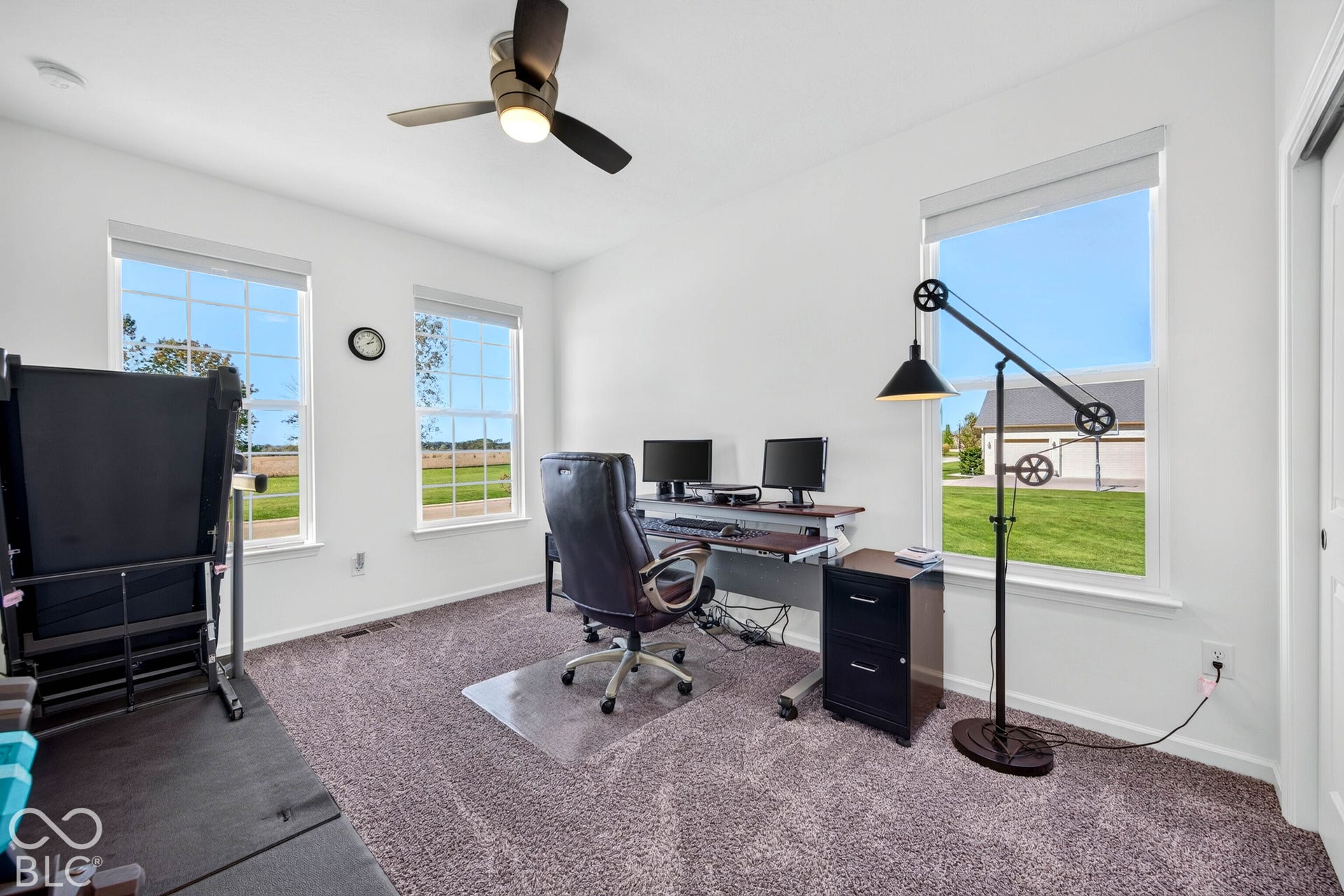 Bright interior room featuring multiple windows, a ceiling fan, and neutral carpeting