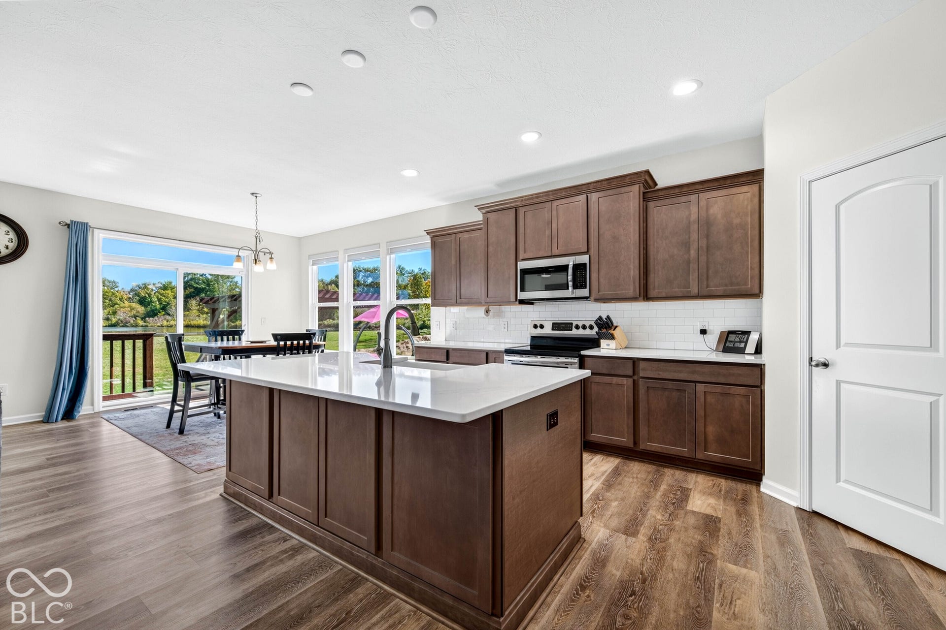 Kitchen with wood-finish flooring, dark wood cabinetry, white subway tile backsplash, and stainless steel appliances