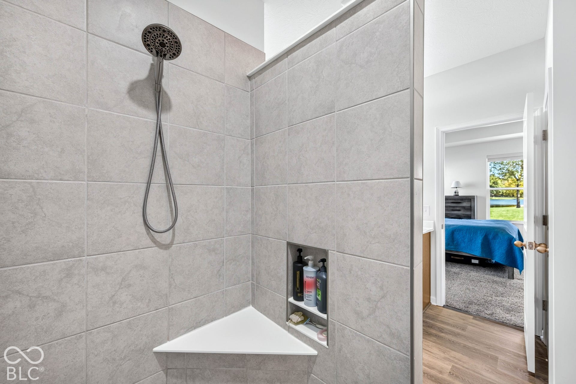 Tiled shower with handheld shower fixture, built-in corner bench, and recessed shelving