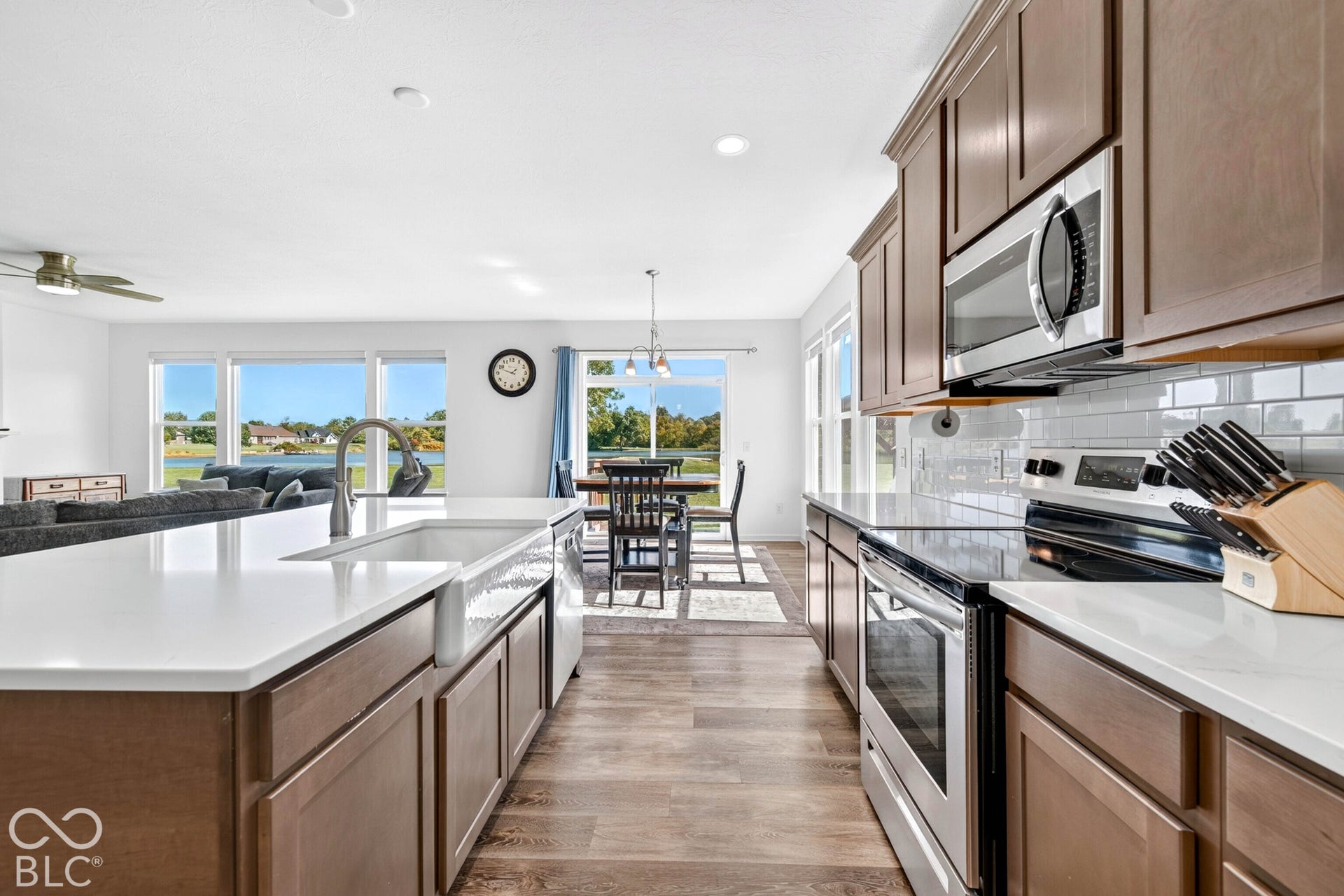 Spacious kitchen featuring an island with a farmhouse sink, stainless steel appliances, wood-finish flooring, and white countertops