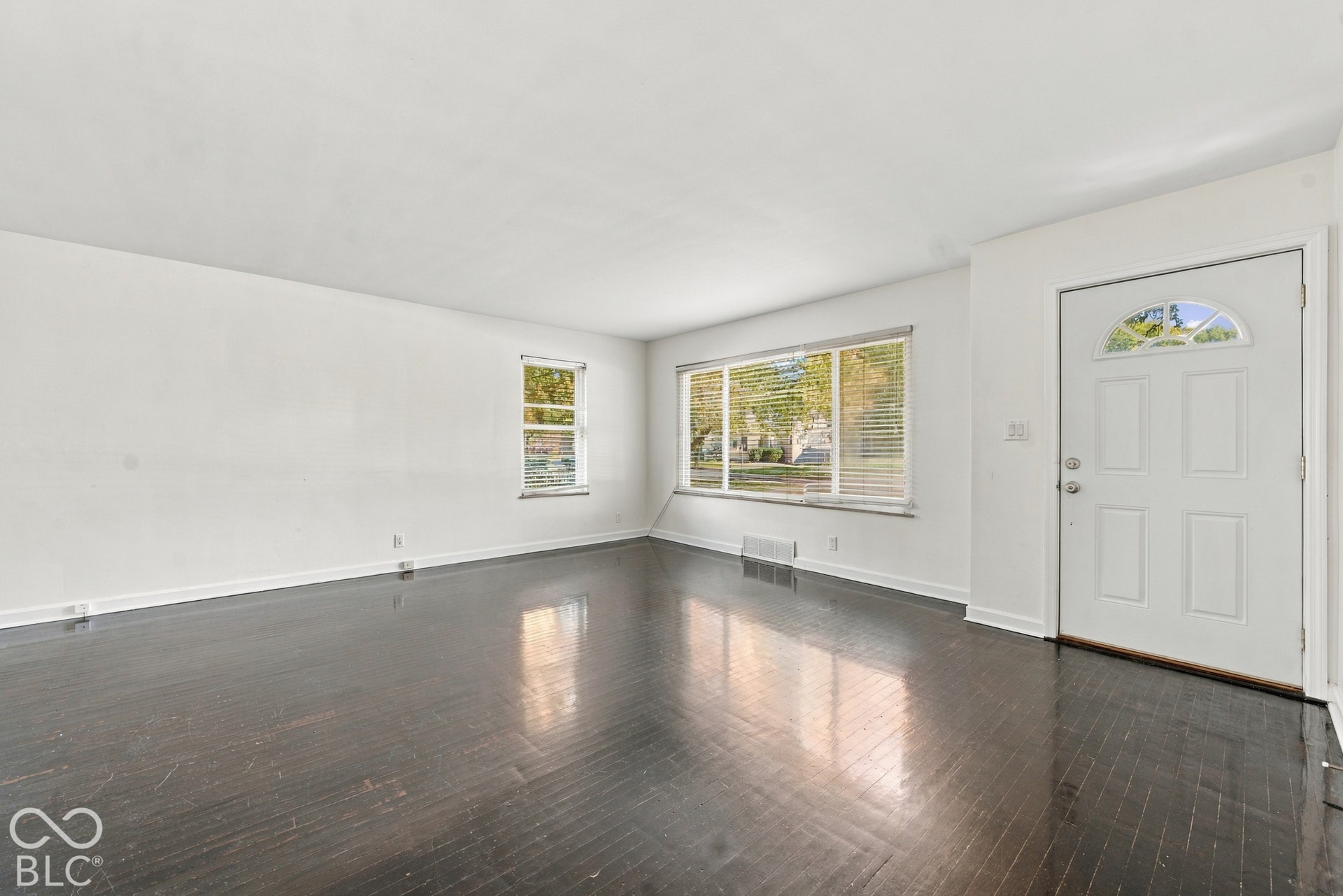 Hardwood flooring, white painted walls, and multiple windows with blinds
