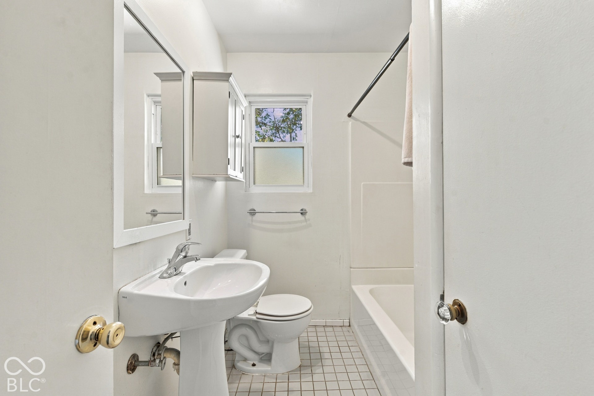 Pedestal sink with chrome faucet, wall-mounted mirror, white framed window, built-in medicine cabinet, and a bathtub with a shower rod