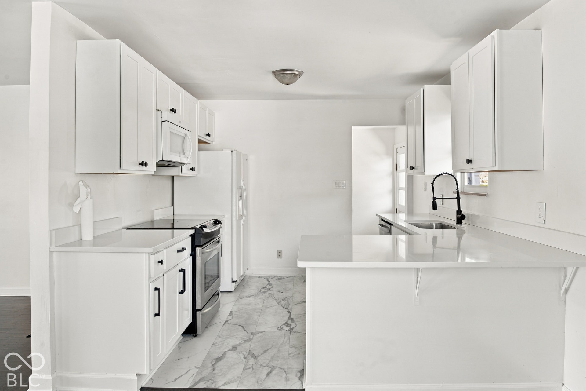 White cabinetry, solid surface countertops, stainless steel appliances, modern black faucet, and patterned flooring