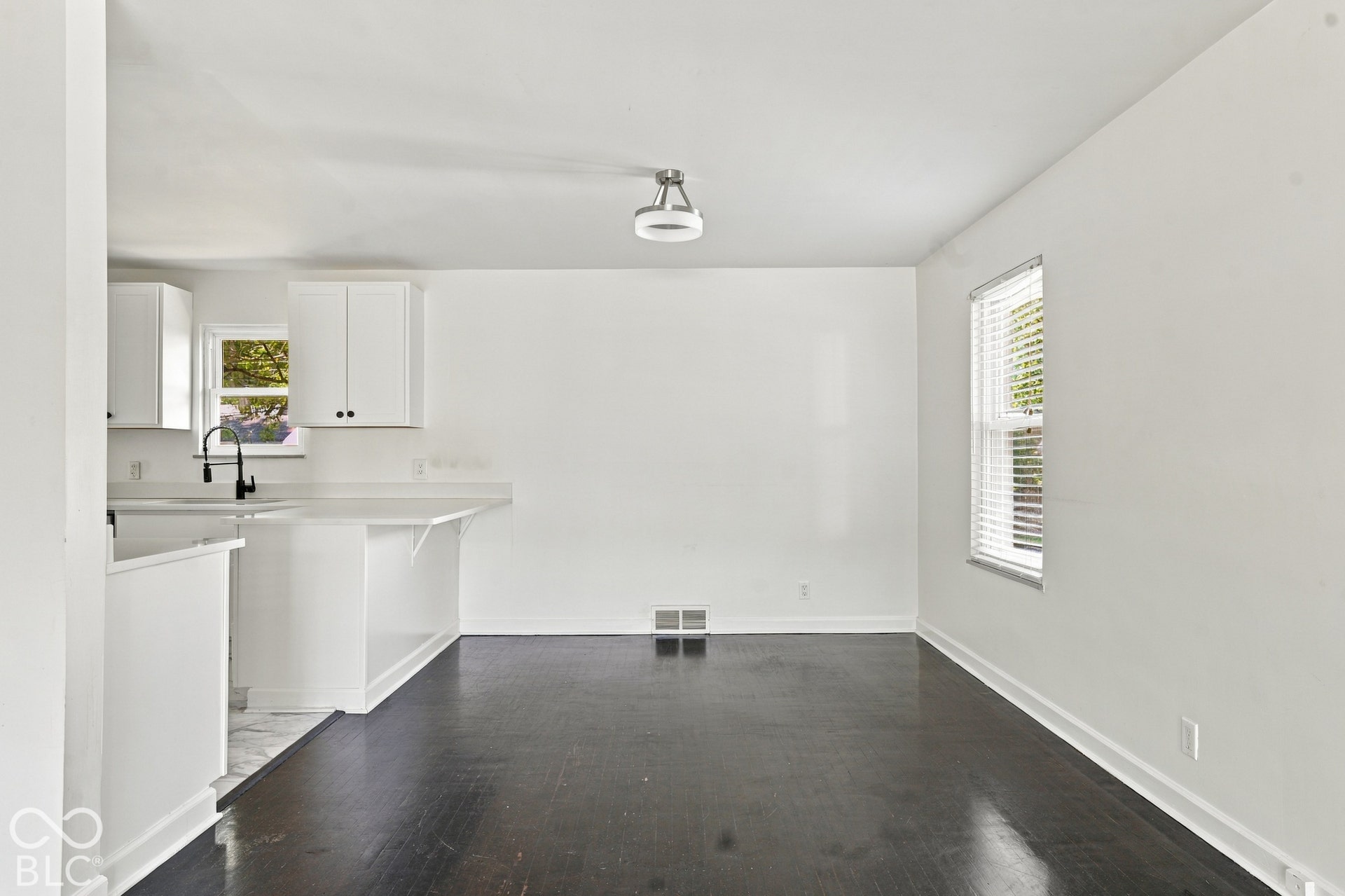 Open-concept living space featuring wood-finish flooring, white walls, and a window with blinds