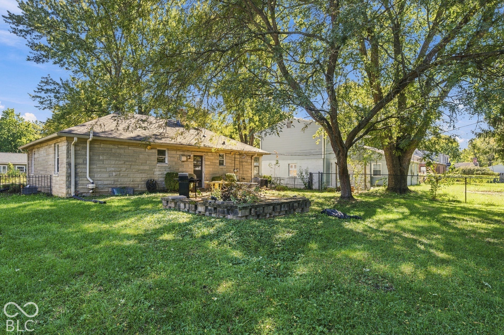 Expansive grassy yard with mature trees, stone-finish exterior, and an outdoor patio area