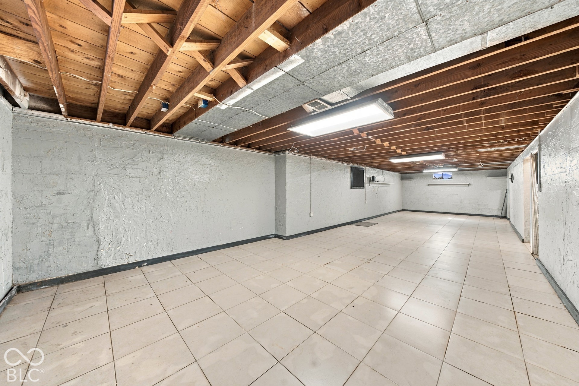 Spacious lower level with exposed ceiling joists, tiled flooring, painted concrete block walls, and recessed lighting
