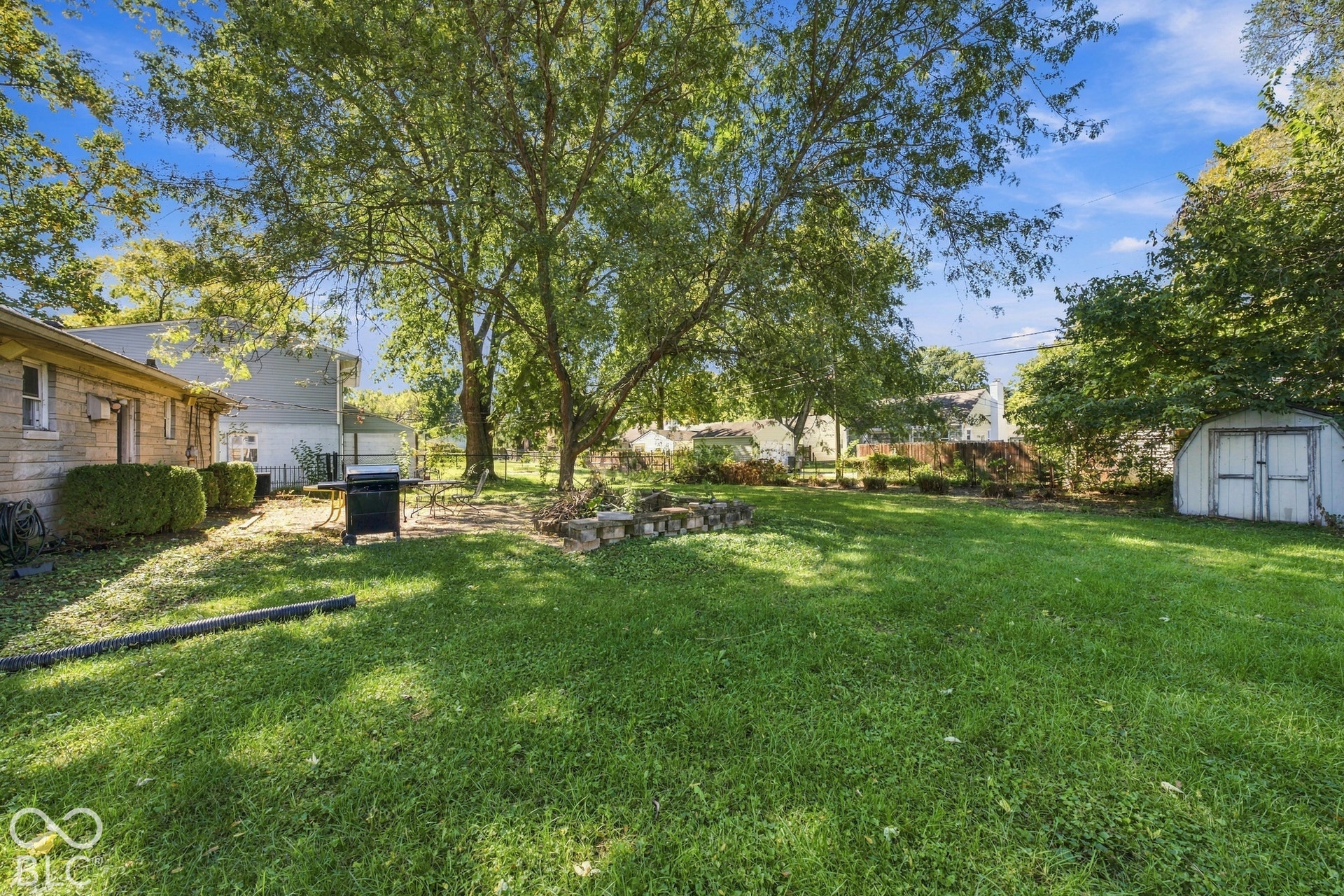 Expansive grassy yard with mature trees, a stone patio area, and a storage shed