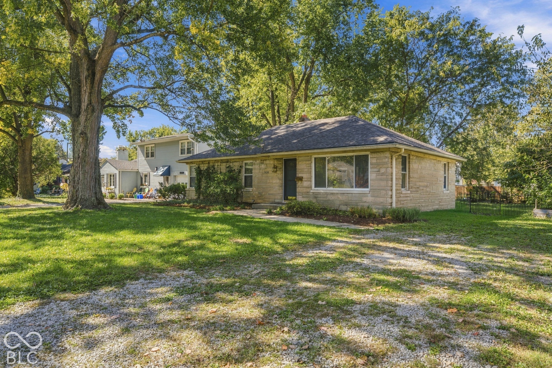 Stone exterior residence with a shingled roof, mature trees, and a gravel driveway