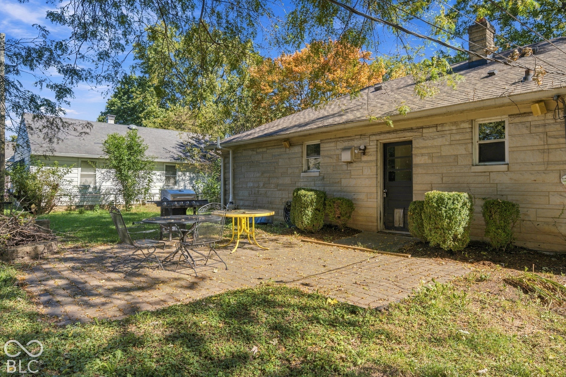 Paved stone patio featuring shrubbery landscaping, a side entry door, and a stone facade