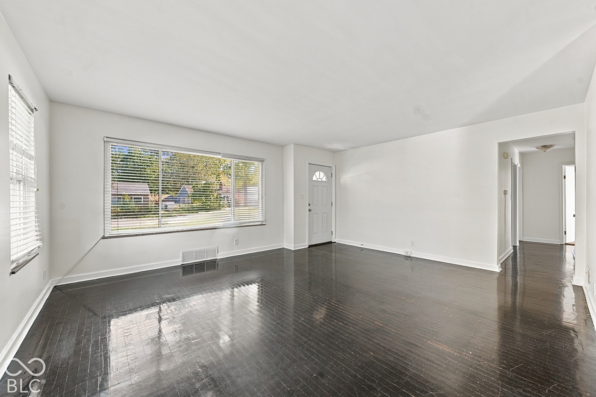 Spacious room featuring dark wood-finish flooring, white walls, and a multi-pane window with blinds