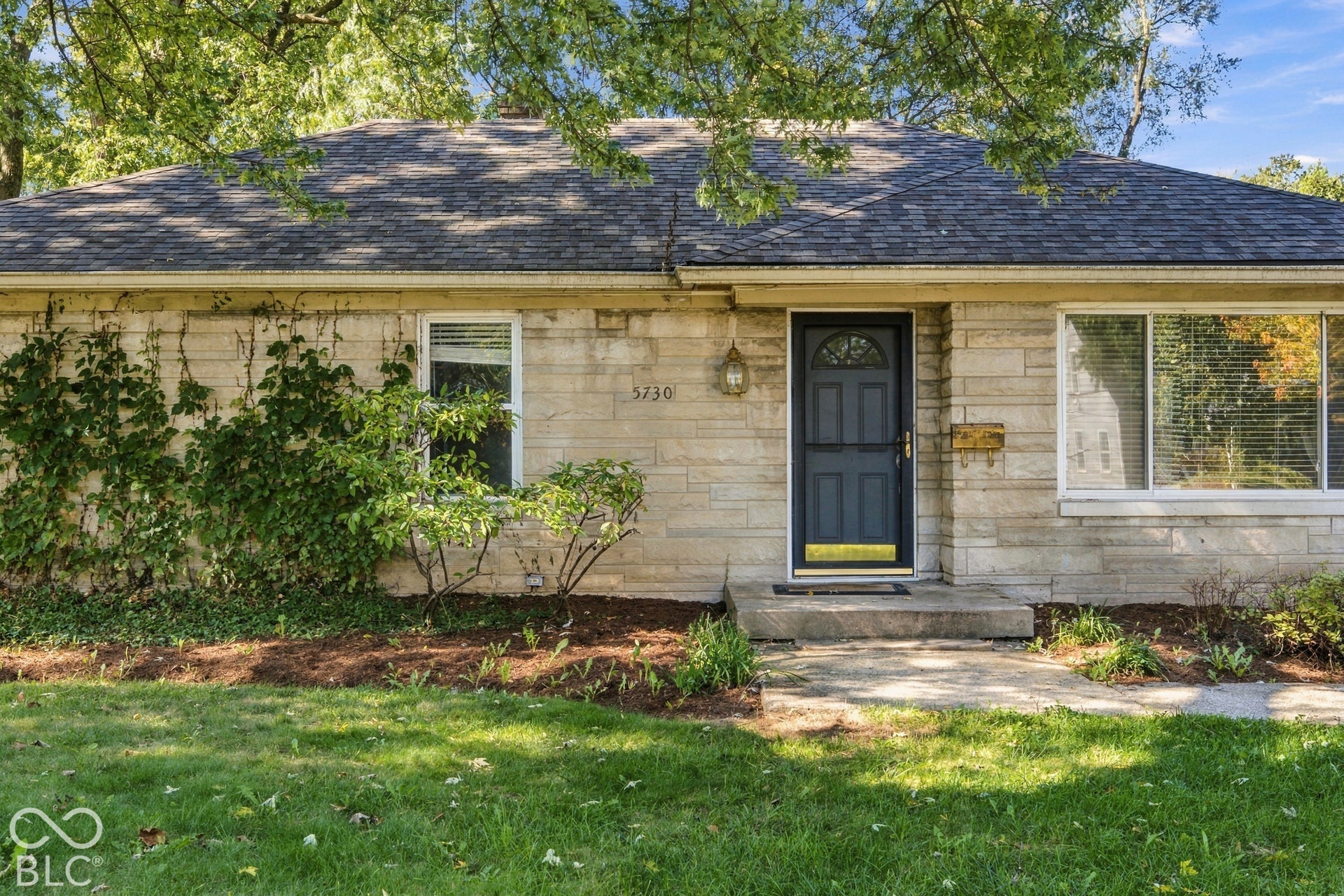 Stone veneer exterior with a dark-paneled entry door, a prominent front window, and a concrete walkway