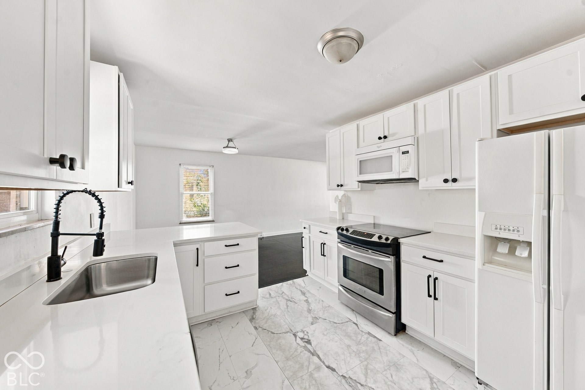 Kitchen featuring white cabinetry with black hardware, stainless steel sink with a matte black faucet, white countertops, and white tile flooring