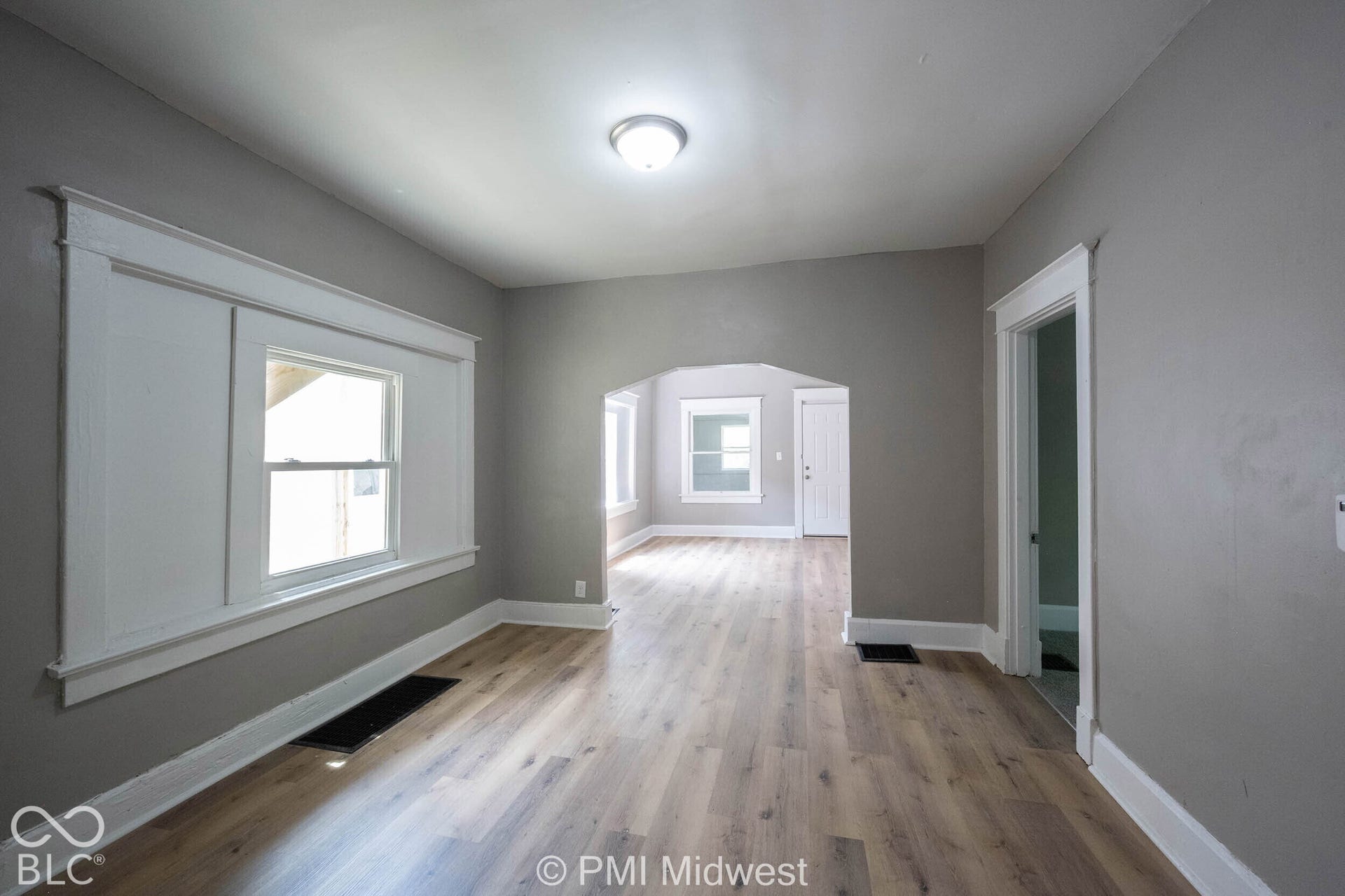 Wood-finish flooring, neutral wall tones, arched doorway, white trim, and a flush mount ceiling light