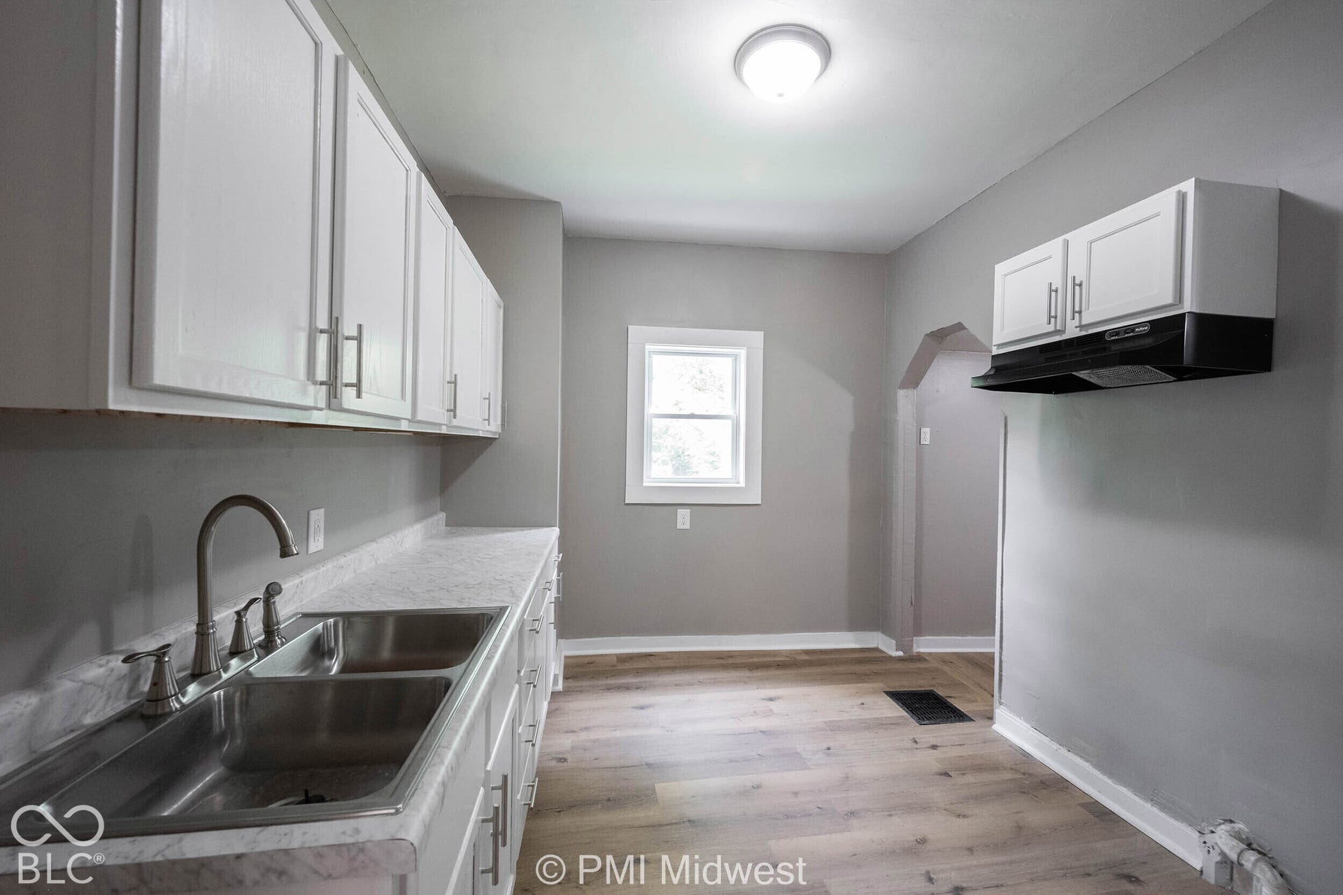 White cabinetry with brushed nickel hardware, double basin stainless steel sink, wood-finish flooring, and a single window