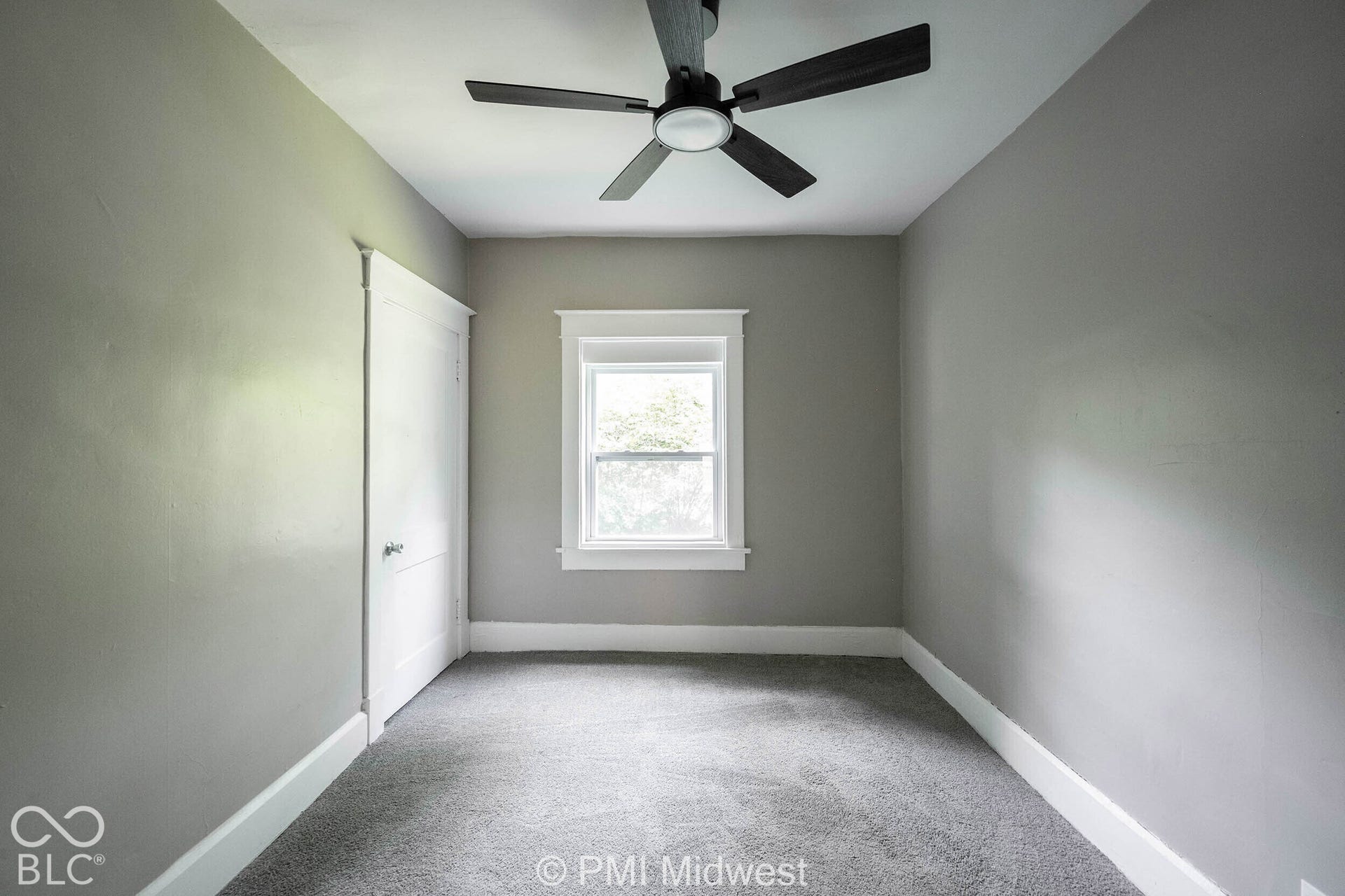 Neutral-toned wall paint, white trim, recessed window, dark ceiling fan with integrated lighting, and gray carpet flooring