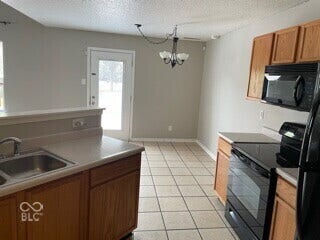 Kitchen featuring tile flooring, wood-finish cabinetry, black appliances, a double basin sink, and a rear exterior door